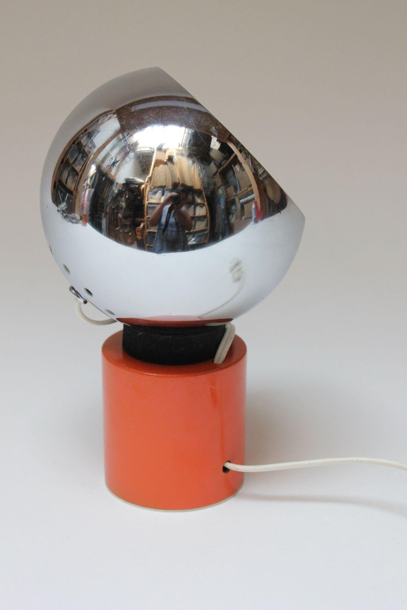 Petite desk/table lamp designed by Luigi Argenta for Reggiani (ca. 1970s, Italy). Composed of a chrome 'eye-ball' fixture supported by a magnetic black and orange base. The magnetic function allows the fixture to maintain its stability after the