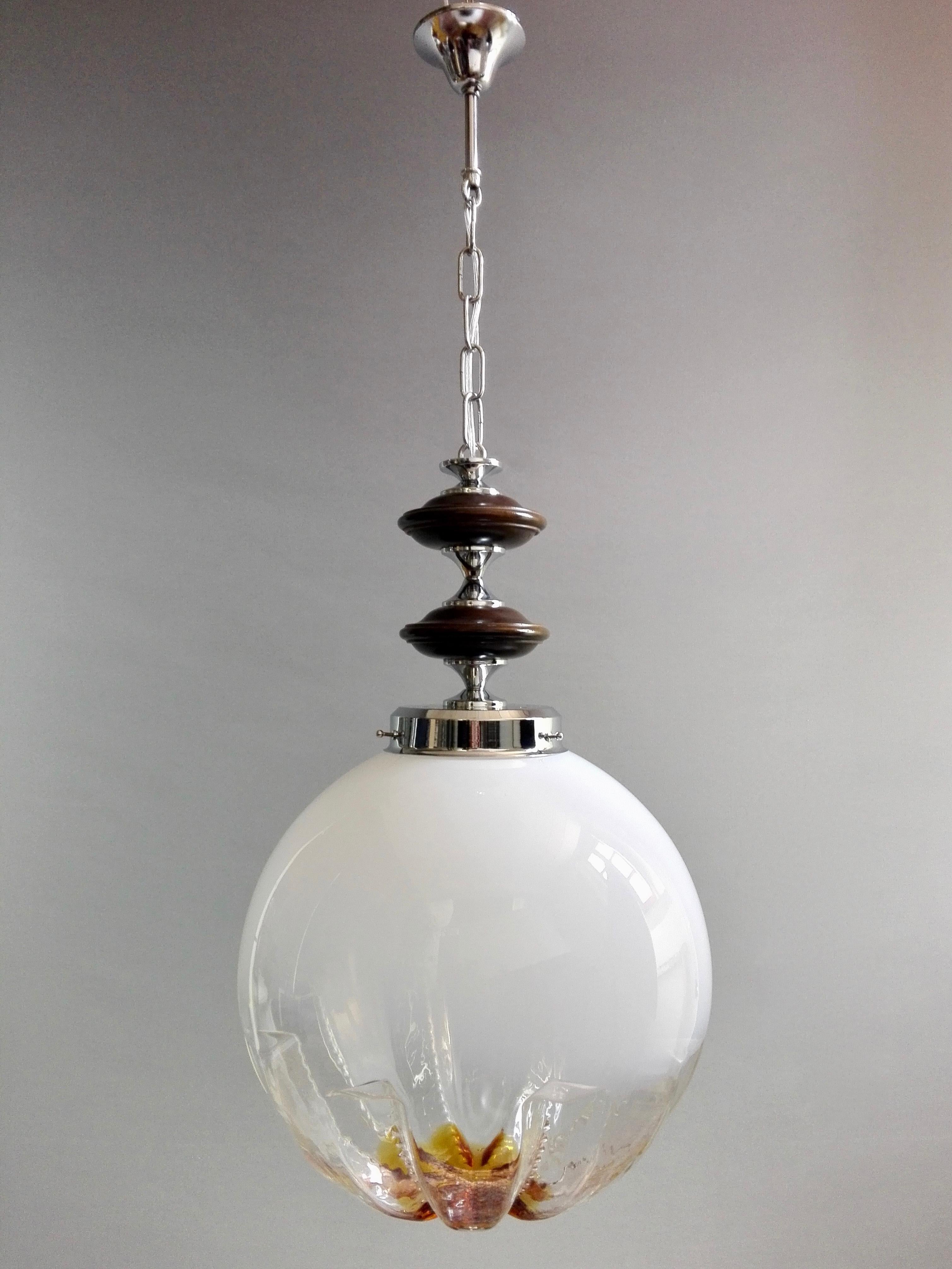 A beautiful large Italian 1970s Space Age one-light Mazzega attributable pendant lamp.
The light has a chrome structure with wooden elements and a really nice clear/milky white Lattimo and amber/orange Murano art glass lampshade. 
The so called