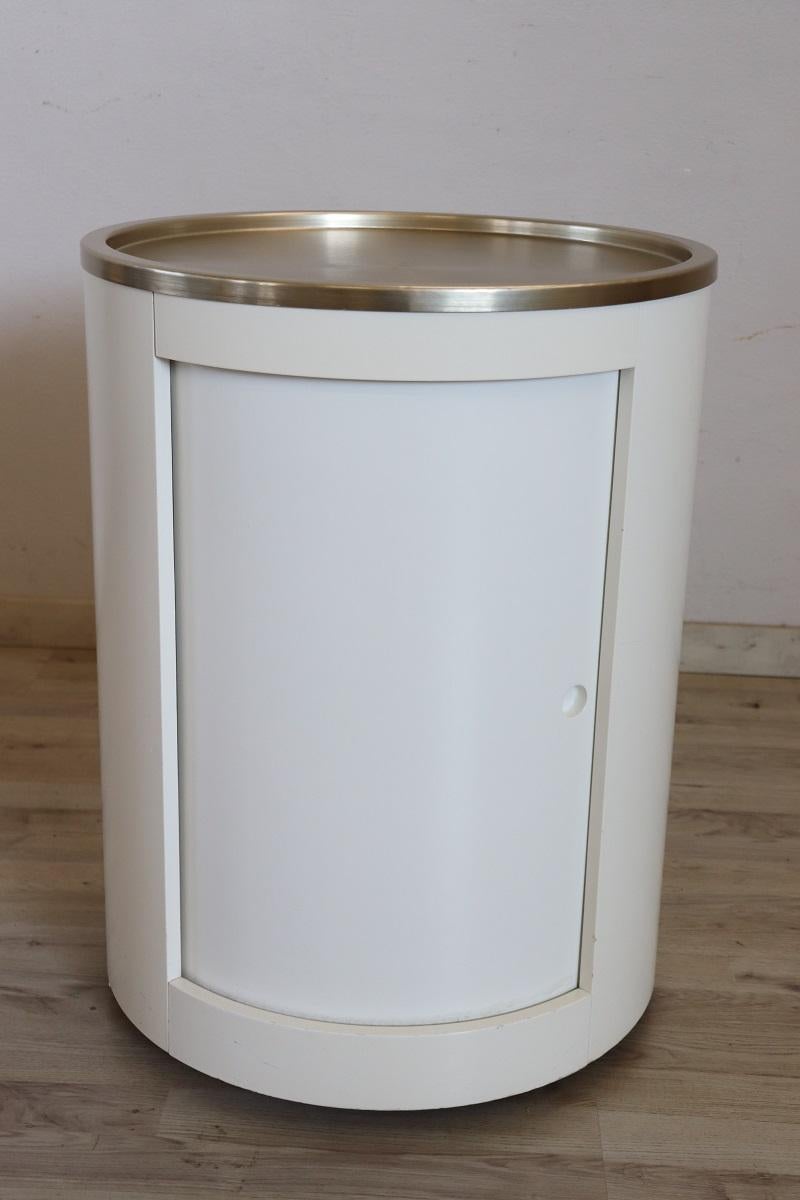 Raro carrito de bar de diseño italiano de la era espacial de los años 60. Se caracteriza por su forma cilíndrica, de madera lacada en blanco y tapa de acero satinado. Equipado con una puerta corredera y un portabotellas en el interior con capacidad