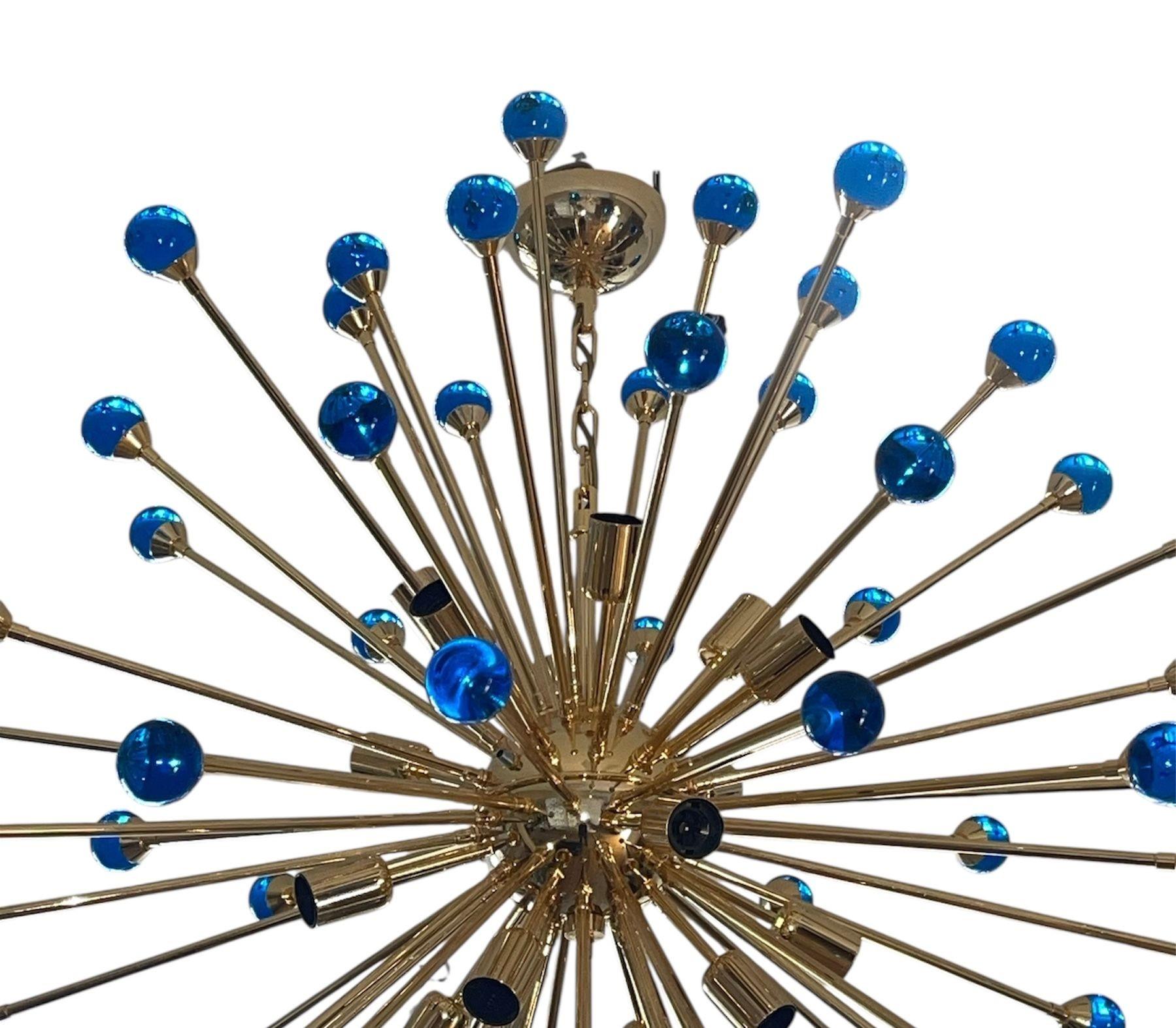 Magnifique lustre Sputnik italien composé de nombreuses sphères en verre de Murano bleu cobalt soufflées à la main et rayonnant à partir d'une armature en métal et de tiges plaquées or 24 carats.
Les éléments en verre vibrant associés à la structure
