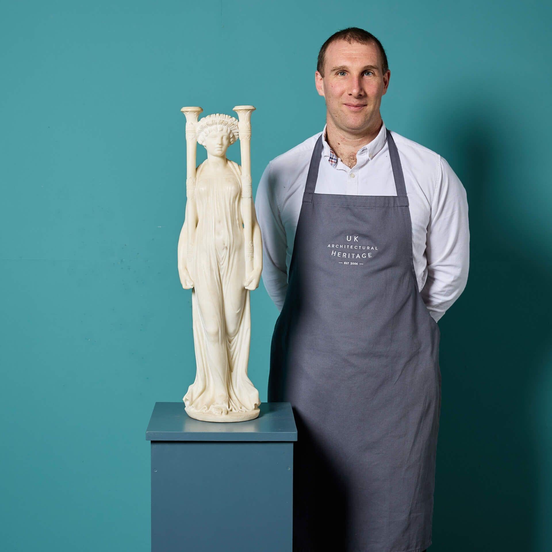 Scultura in marmo statuario italiano della fine del XIX secolo raffigurante una fanciulla neoclassica che indossa un copricapo e porta due torce cerimoniali o portabandiera come se fosse in processione. Si tratta di un soggetto raro e insolito,