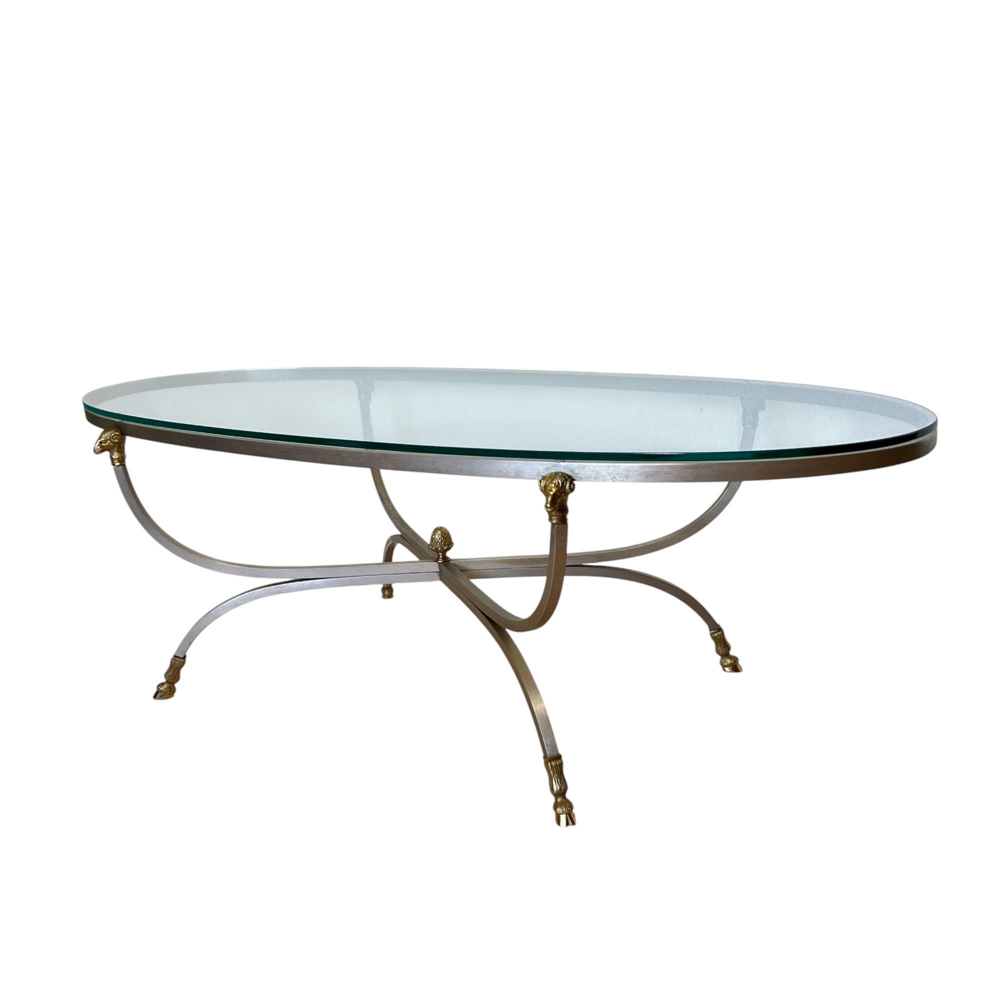 Table basse ovale en acier et laiton de style Maison Jansen du milieu du siècle dernier, circa 1960. Elegant et intemporel, il se compose d'un cadre en acier moderne et élégant, d'une tête de bélier, d'un sabot et d'un fleuron central en laiton,