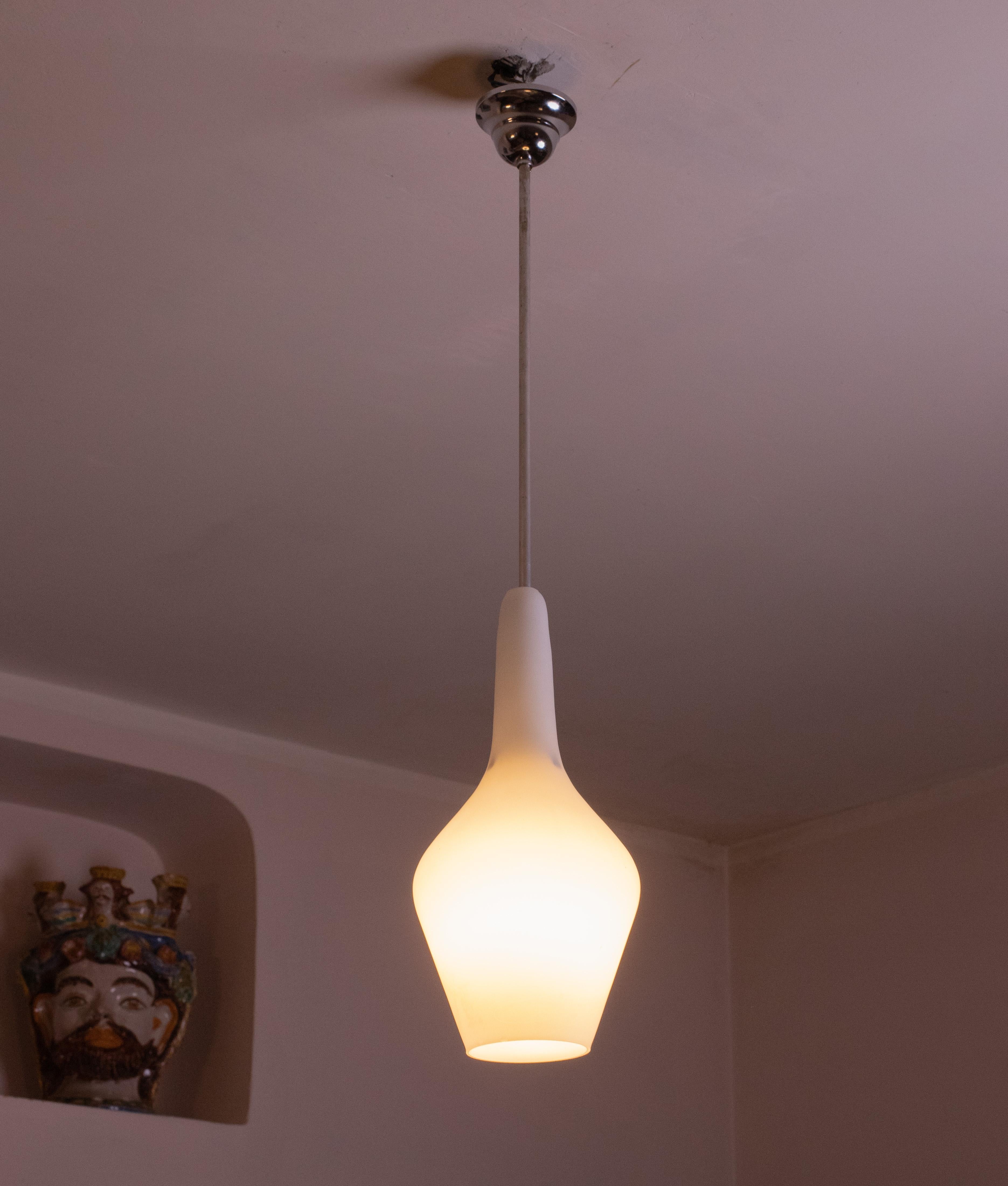 Stilnovo design opaline glass pendant made in the 1970s.
It connects to the ceiling with a brass element; the wire cover rosette has been replaced.
The cap is made of white opaline glass, attached to the structure by an aluminum element. The