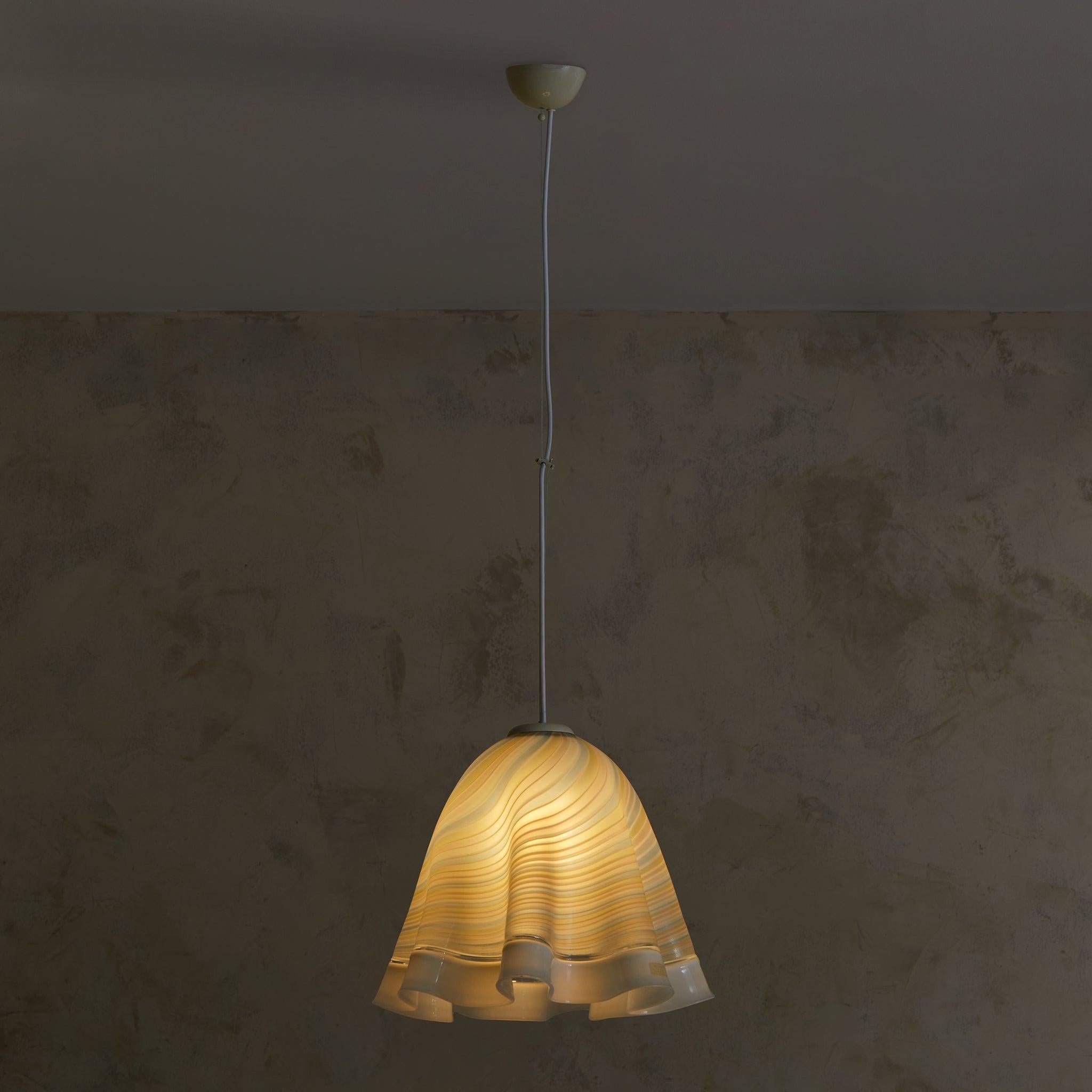 Cette suspension en verre de Murano est un reflet élégant de l'art italien des années 1970, mettant en valeur des lignes fluides et un savoir-faire magistral. Son abat-jour soufflé à la main, aux bords ondulés, met en valeur de délicates teintes