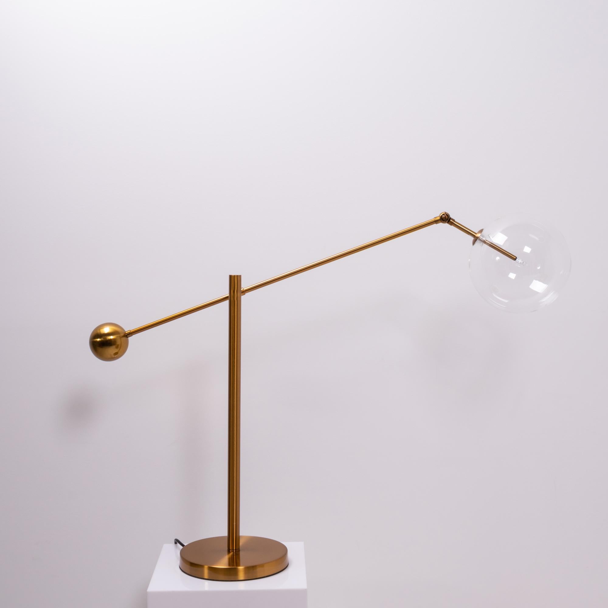 Inspired by Mid Century Italian design, this table lamp features a striking globe shade in clear glass.

Sitting on a round brass base, the arm cantilevers off of the stand and is weighted at the end with a brass sphere.

The lamp has a UK plug