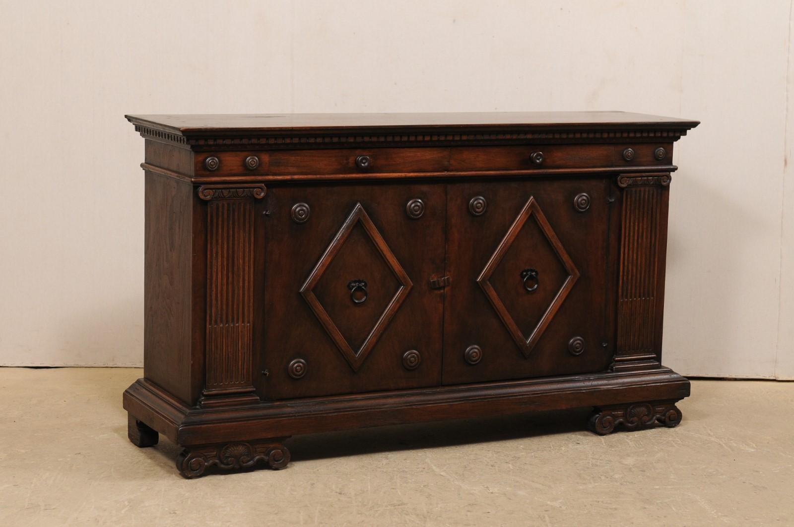 An Italian style carved wood credenza from the mid-20th century. This vintage American-made cabinet of rich, walnut wood is rectangular-shaped, with a slightly overhanging top which is beautifully decorated with stacked molding and dentil trim