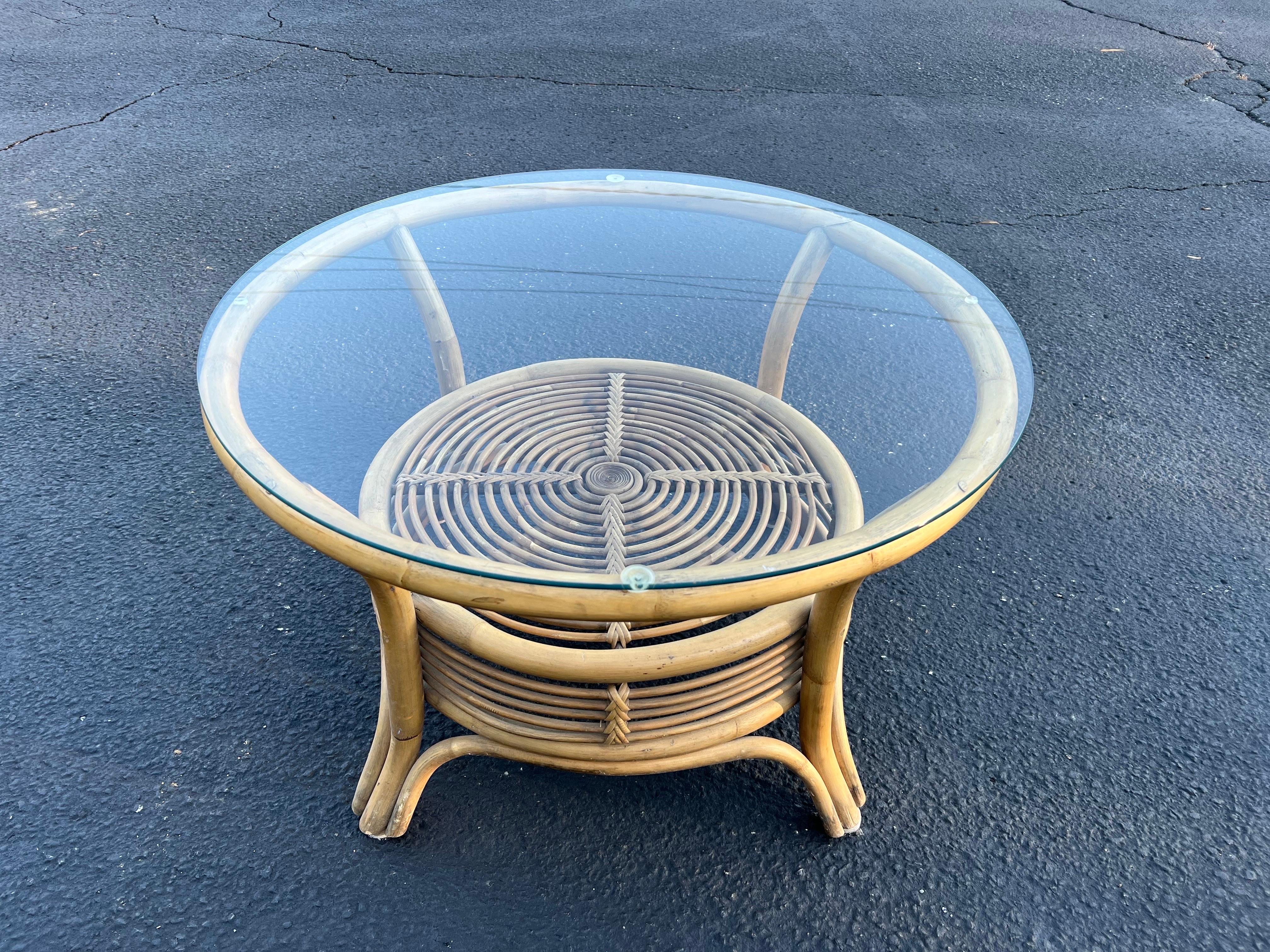Italian style rattan and bamboo coffee table with glass top. Nice round two tiered table use as a side table or as a smaller coffee table. Swirling weaved design. Nice for that coastal beach home vibe.