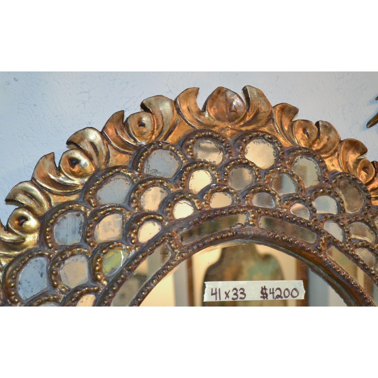 Magnificent Italian Hollywood Regency style cabochon-shaped oval mirror. The ornate giltwood frame with a finely carved foliate border, the central mirror surrounded by tiers of small inlaid glass and mirror accents,

circa 1940.