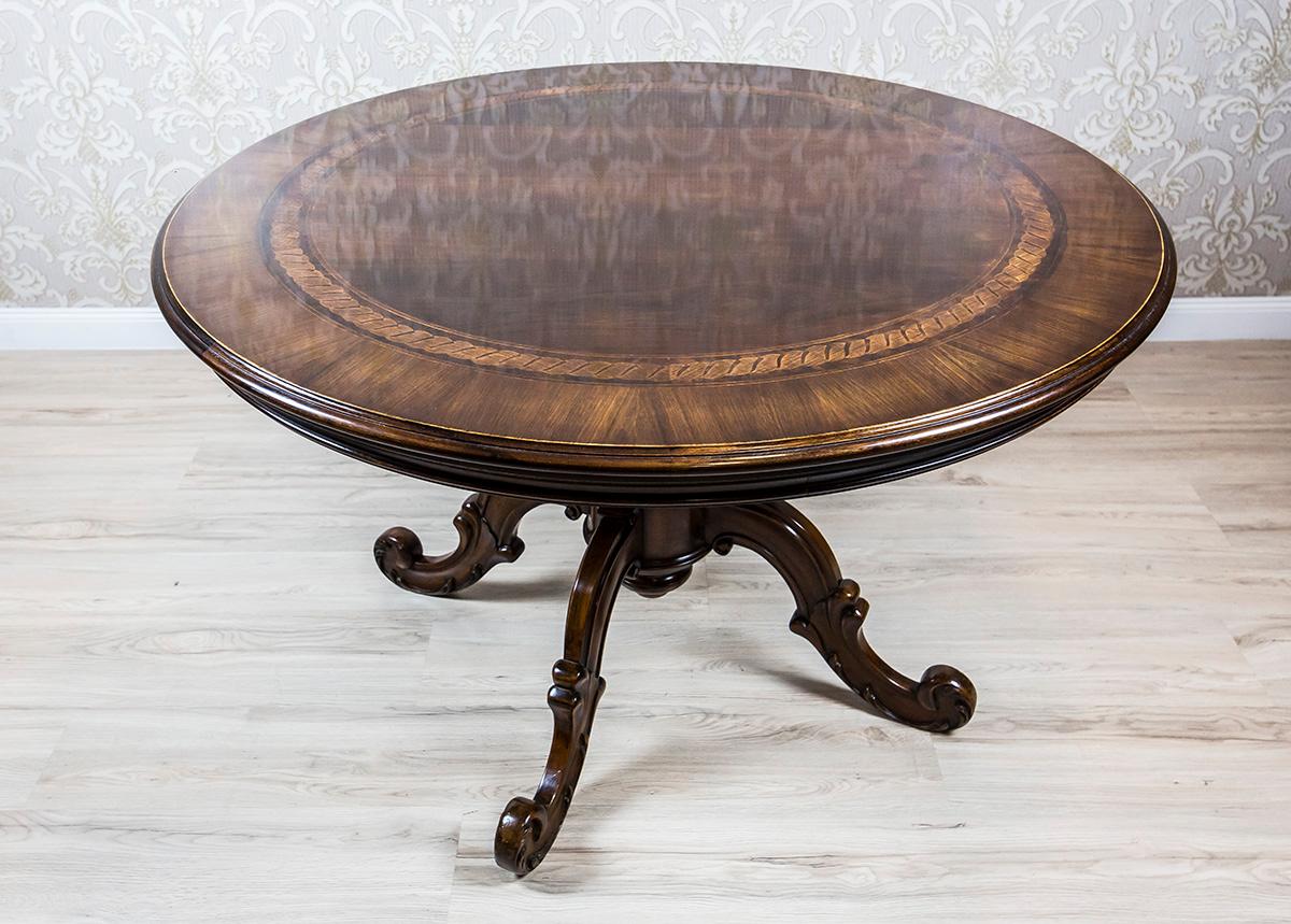 Wir präsentieren Ihnen diesen massiven, runden Esstisch aus Holz aus den 1960er Jahren.
Die runde Tischplatte ruht auf einem gedrechselten Sockel mit einem vierzackigen Fuß mit Volutenfüßen.
Außerdem ist das Oberteil mit einem Streifen