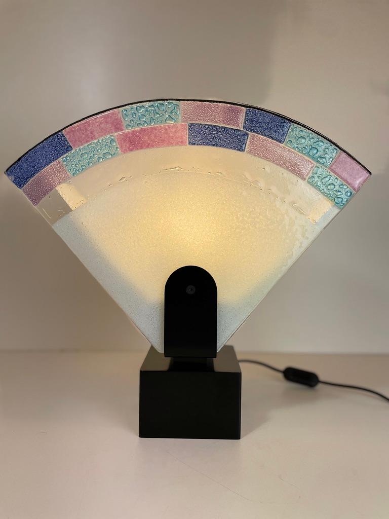 Tischleuchte Serie 6000-7500 von Zonca.
Das Design dieser Lampe ist ein typisches Beispiel für den postmodernen Stil der 1980er Jahre.
Das Murano-Glas in Fächerform hat die Pastellfarben der damaligen Zeit, nicht zu vergessen die schwarze Basis aus