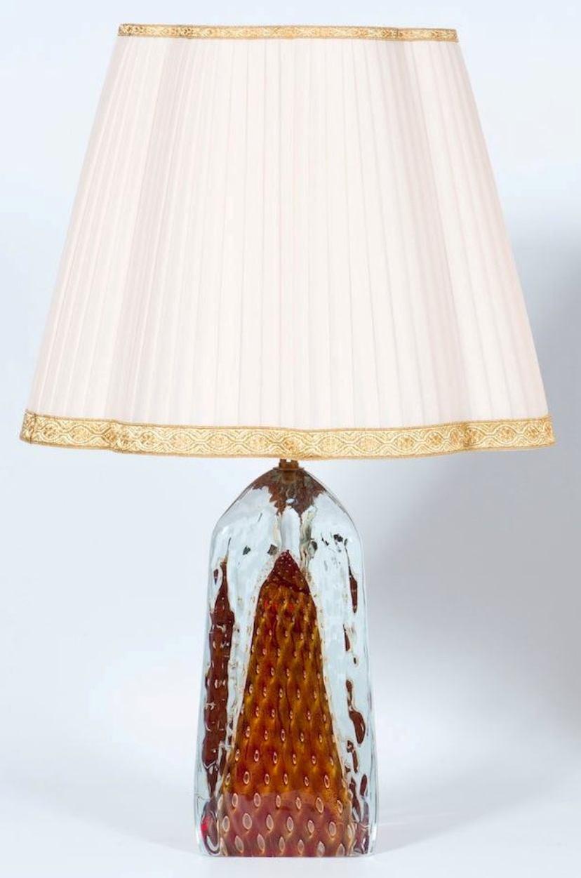 Eine anmutige Tischlampe aus rubinrotem Murano-Glas mit Goldverzierungen aus den 1990er Jahren, Italien.
Diese bezaubernde Tischleuchte, die vollständig aus Murano-Glas handgefertigt ist, verkörpert die Kunstfertigkeit und das handwerkliche Können