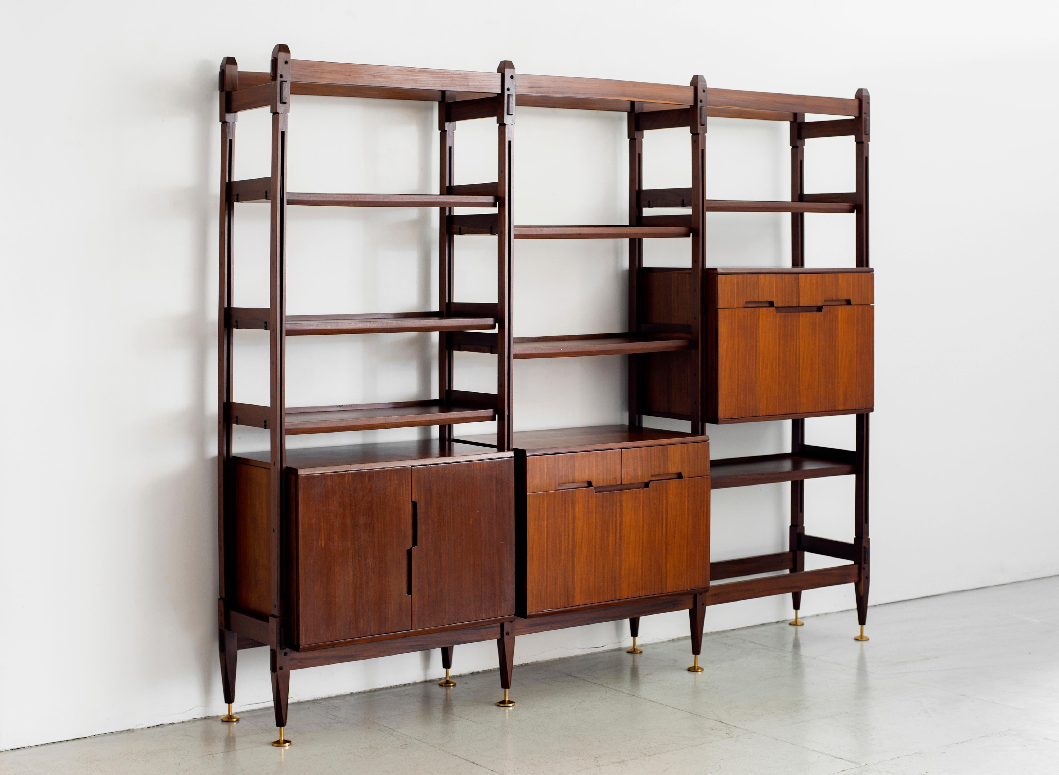 1960s Italian teak free floating wall unit / bookcase with multiple shelves and compartments for storage. 
Fantastic over sized brass feet.
Original patina to wood. 

Measures: W 100” x D 16” x H 83.25”.