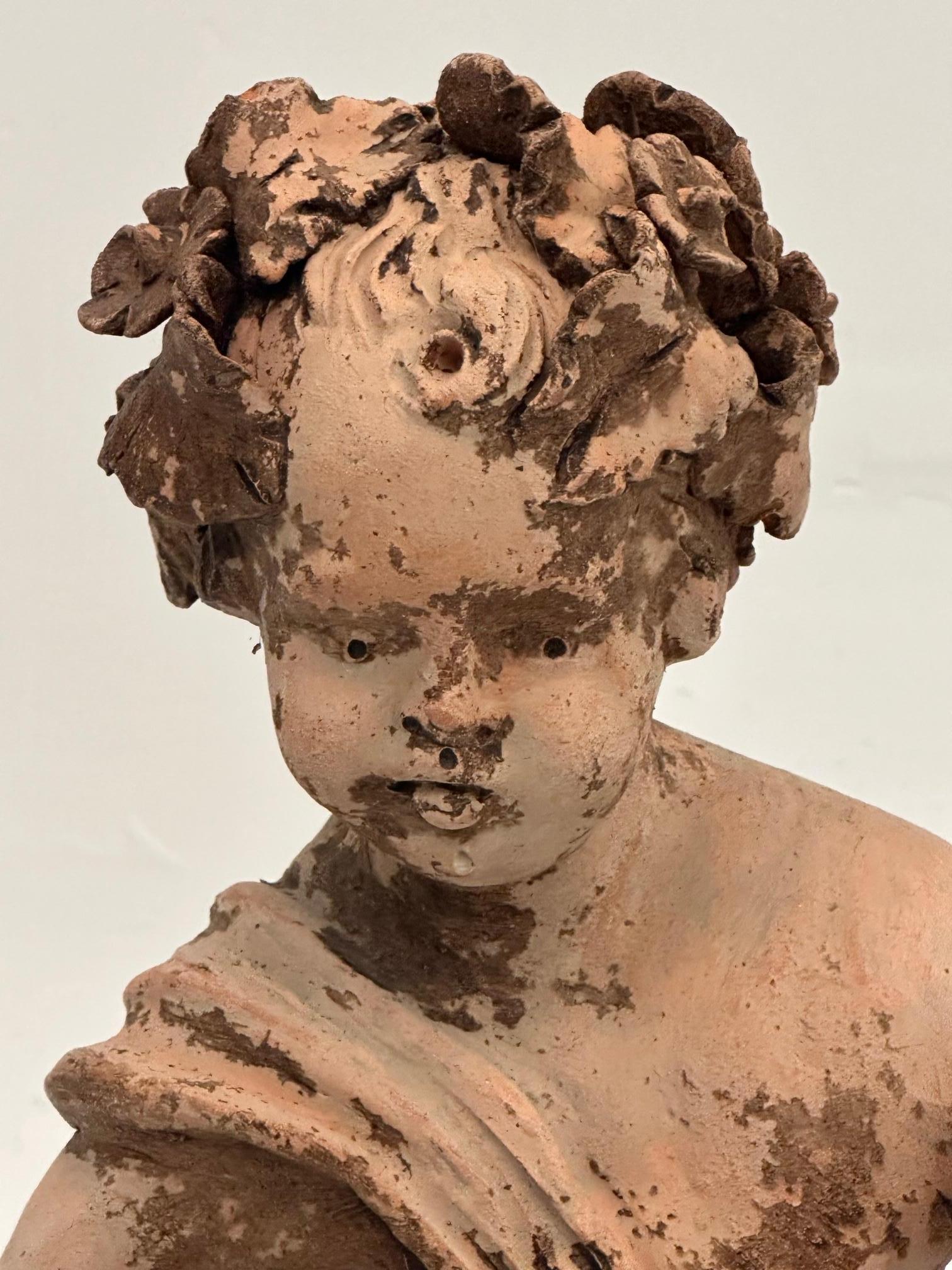 Charming character rich terracotta statue of a cherubic young boy carrying an arrangement of flowers.  Wonderful original distressed patina.