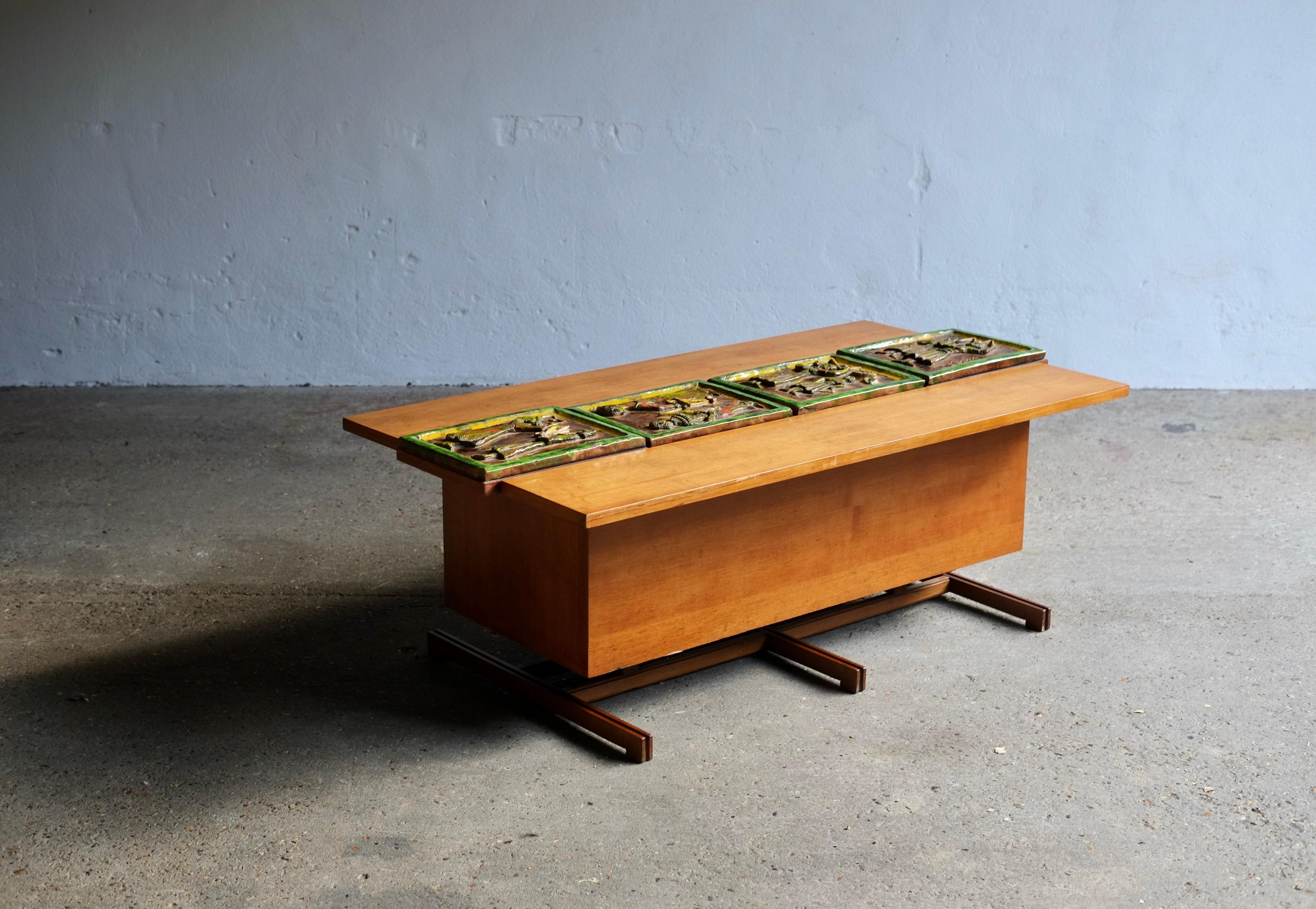 A bespoke wooden midcentury Italian coffee table featuring large signed ceramic tiles which adjust to reveal a cocktail compartment within.
