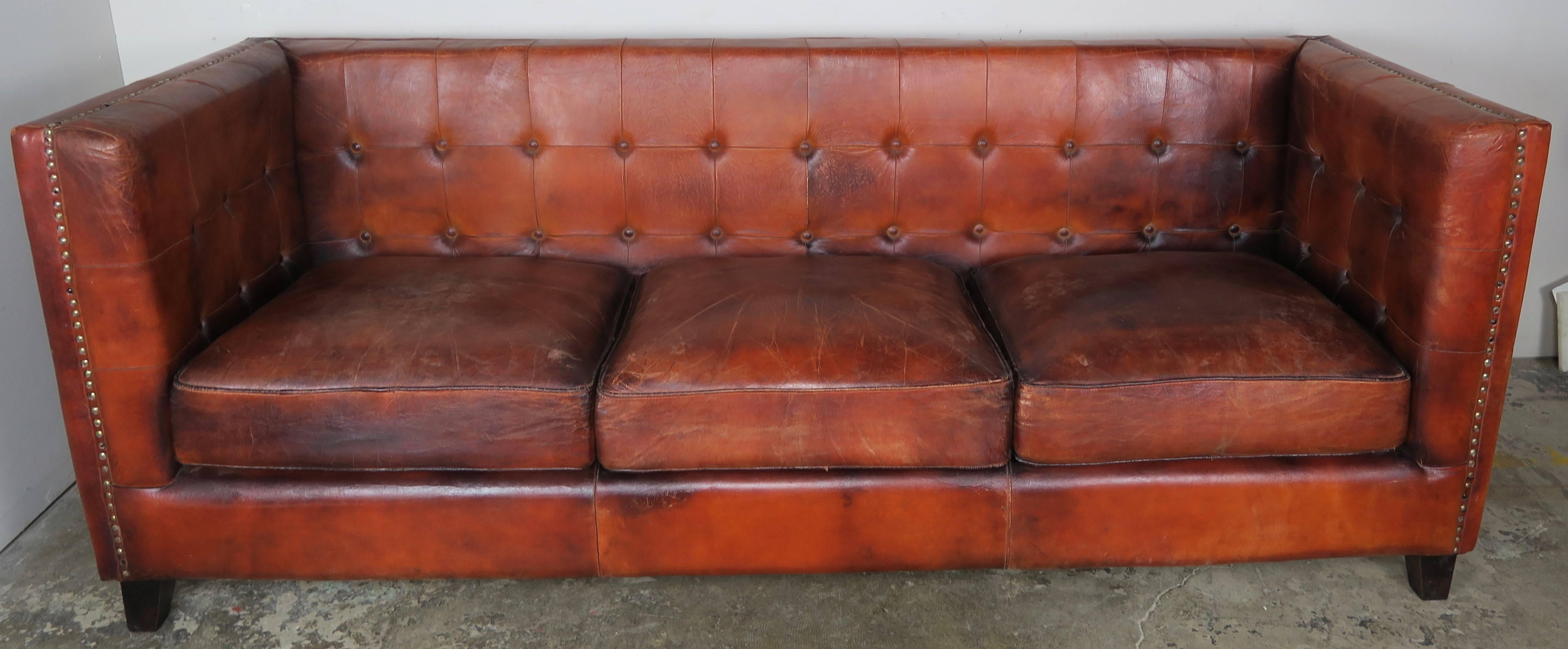 Italian tobacco colored leather sofa with three cushions. The sofa stands on four ebony stained feet with tufted back and sides. Brass nailhead trim detail around the back and down both arms of the sofa. The sofa is in all original condition with
