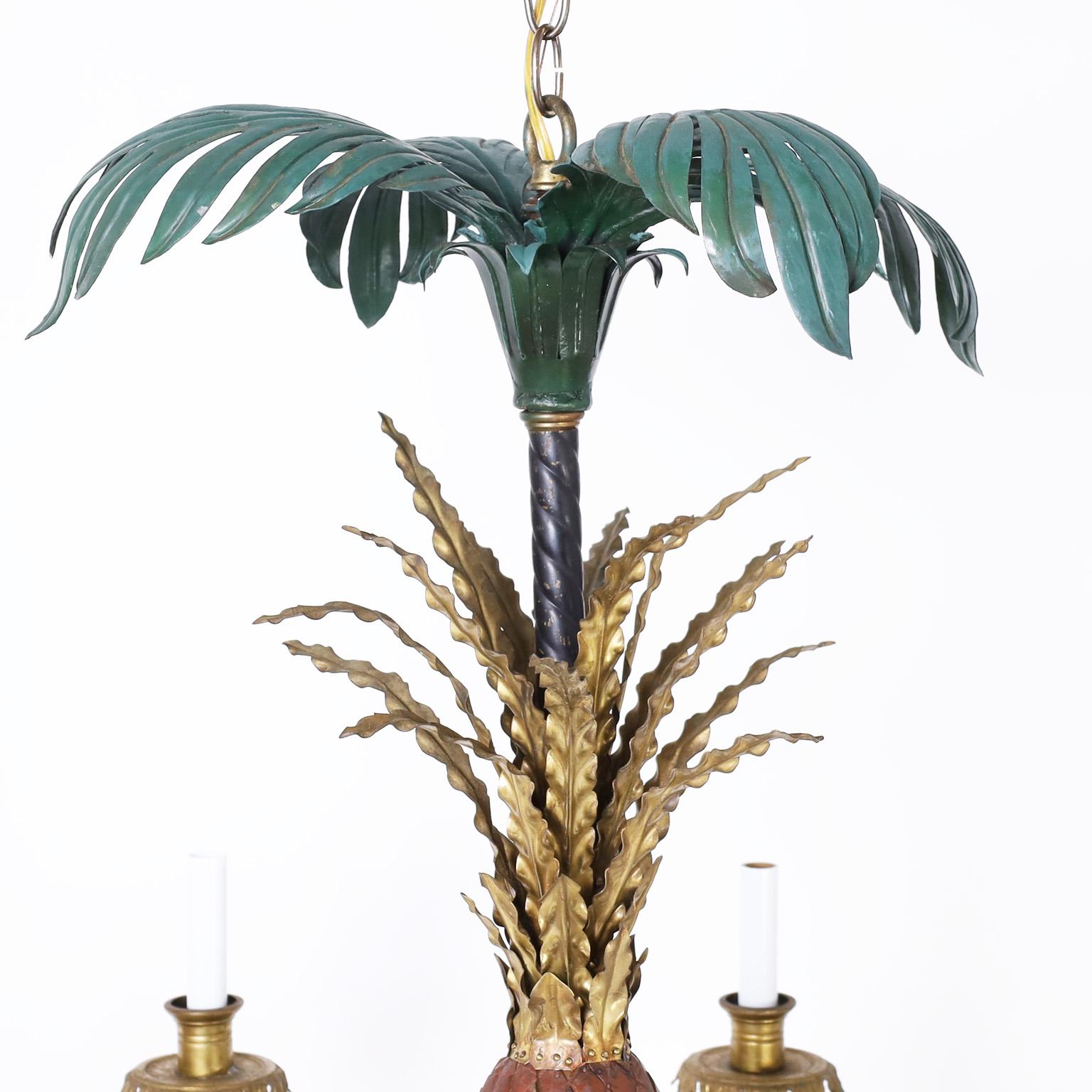 Lustre à huit lumières en laiton et métal peint dans une composition classique avec des feuilles de palmier au sommet sur un ananas tole avec des feuilles en laiton. Les huit bras en forme de feuilles de palmier supportent des douilles en laiton en