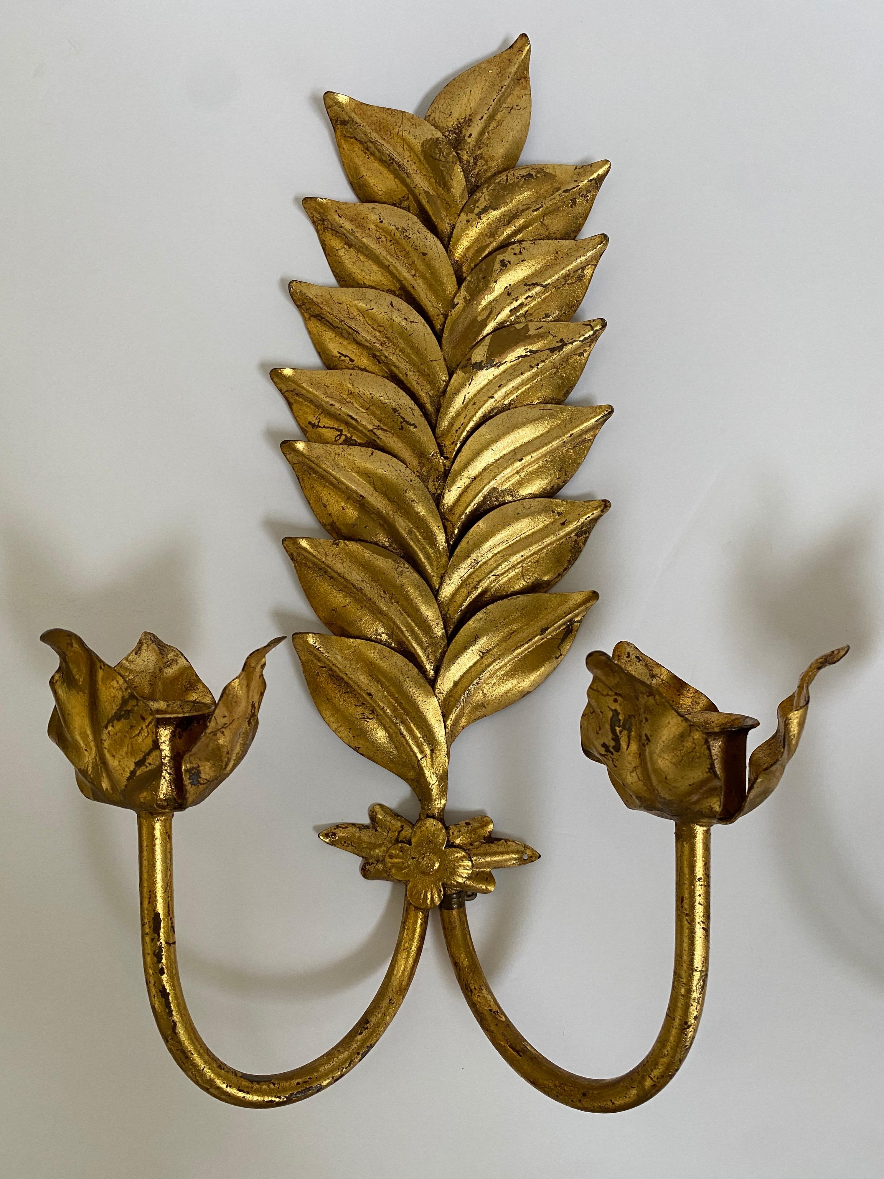 Pair of Hollywood Regency style double arm Laurel leaf motif candle wall sconces. These gold gilt metal botanical foliate sconces hold standard taper candles and retain their original 