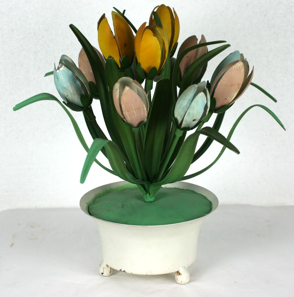 Décoration de table italienne en forme de tulipe en pot, peinte à froid. Un pot à pied blanc contient une grappe symétrique de tulipes fermées en métal de couleur rose, bleue et jaune. Les feuilles sont d'une finition mate d'un riche vert