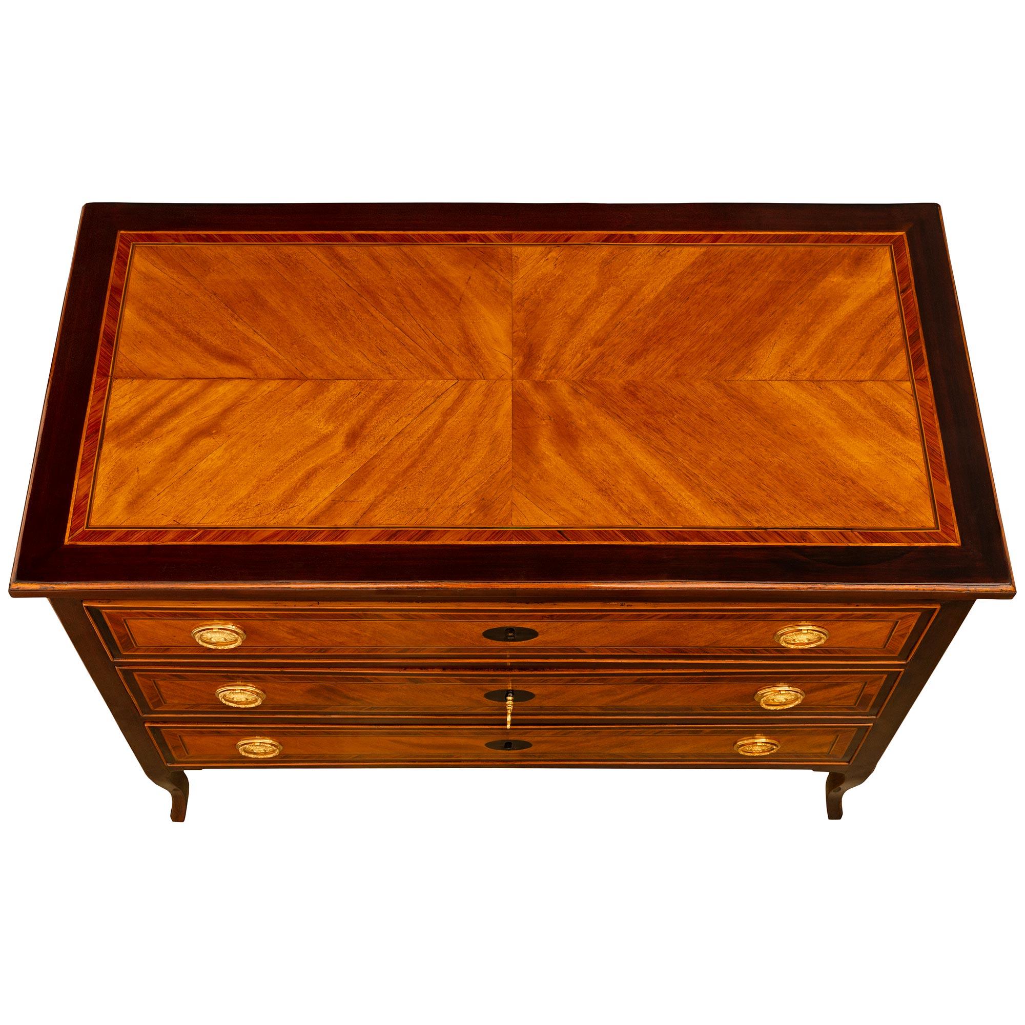A handsome Italian 18th century Transitional period Mahogany, Tulipwood, Cherrywood and Ormolu commode. The three drawer commode is raised by elegant slender tapered cabriole legs below the straight apron and drawers. Each drawer has an central oval