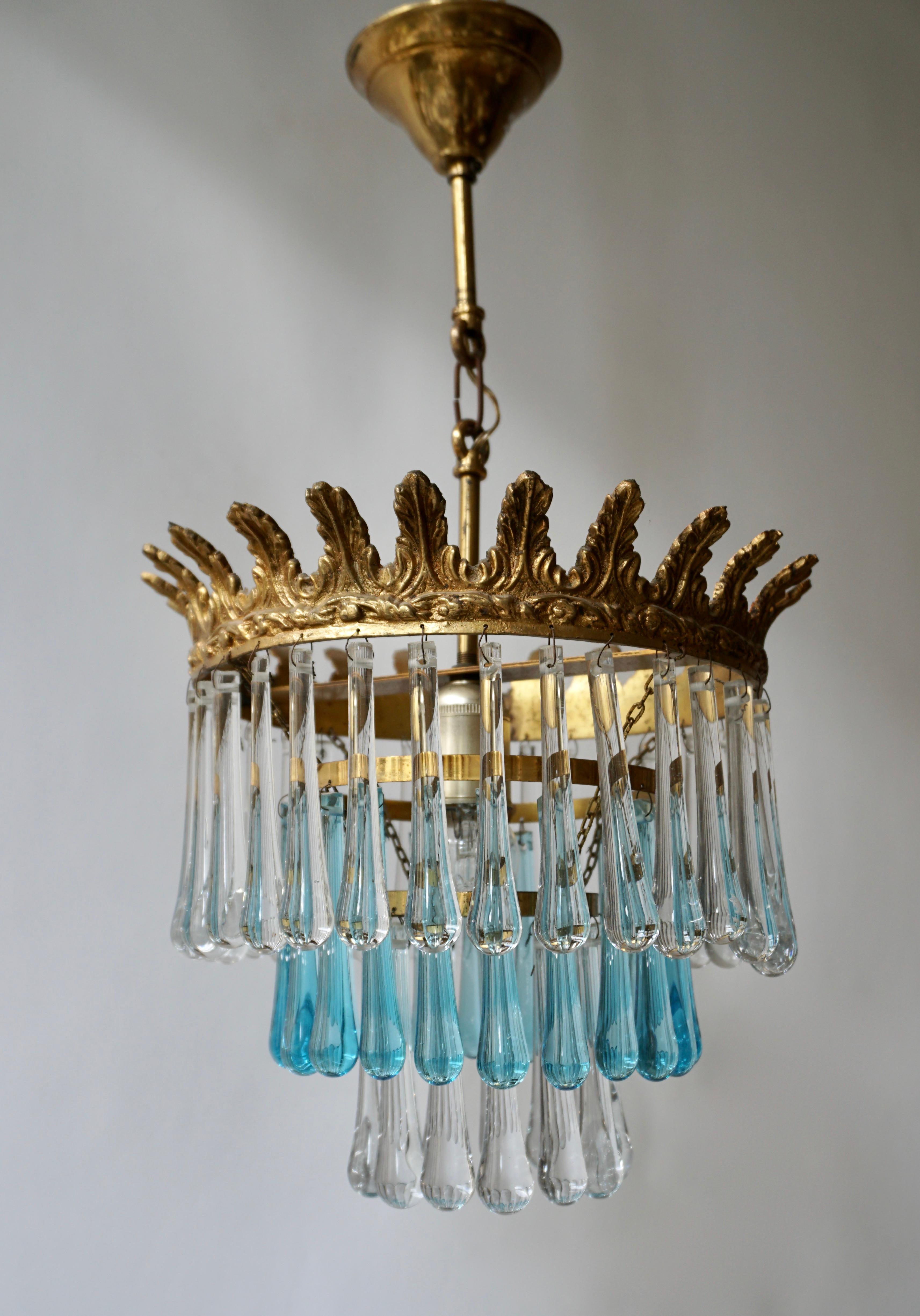 An elegant flushmount or chandelier with blue and transparent crystal teardrop glass segments in a radial pattern.
The result is a very sparkling effect typical of Hollywood style and glamour. The fixture is brass and the glass is hand blown.