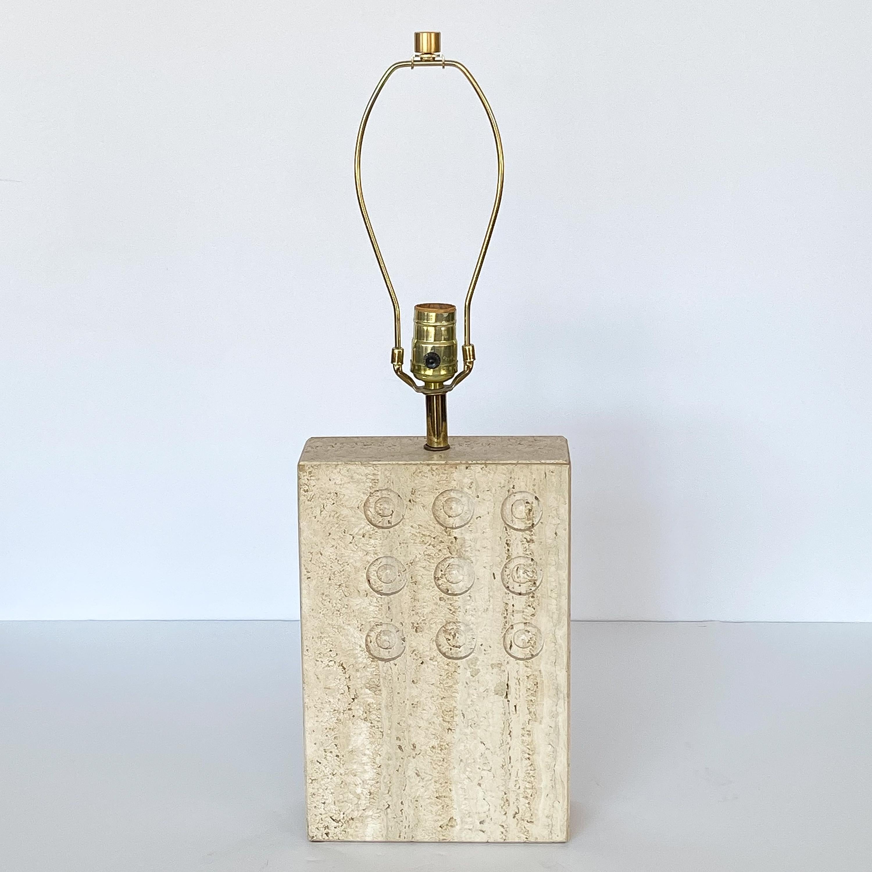 Stunning Italian travertine table lamp by Goffredo Reggiani for Raymor, circa 1960s. Solid travertine lamp with a grid of 9 carved / impressed circular designs. Brass stem, harp and finial. Takes one standard base light bulb. Working condition. Sold