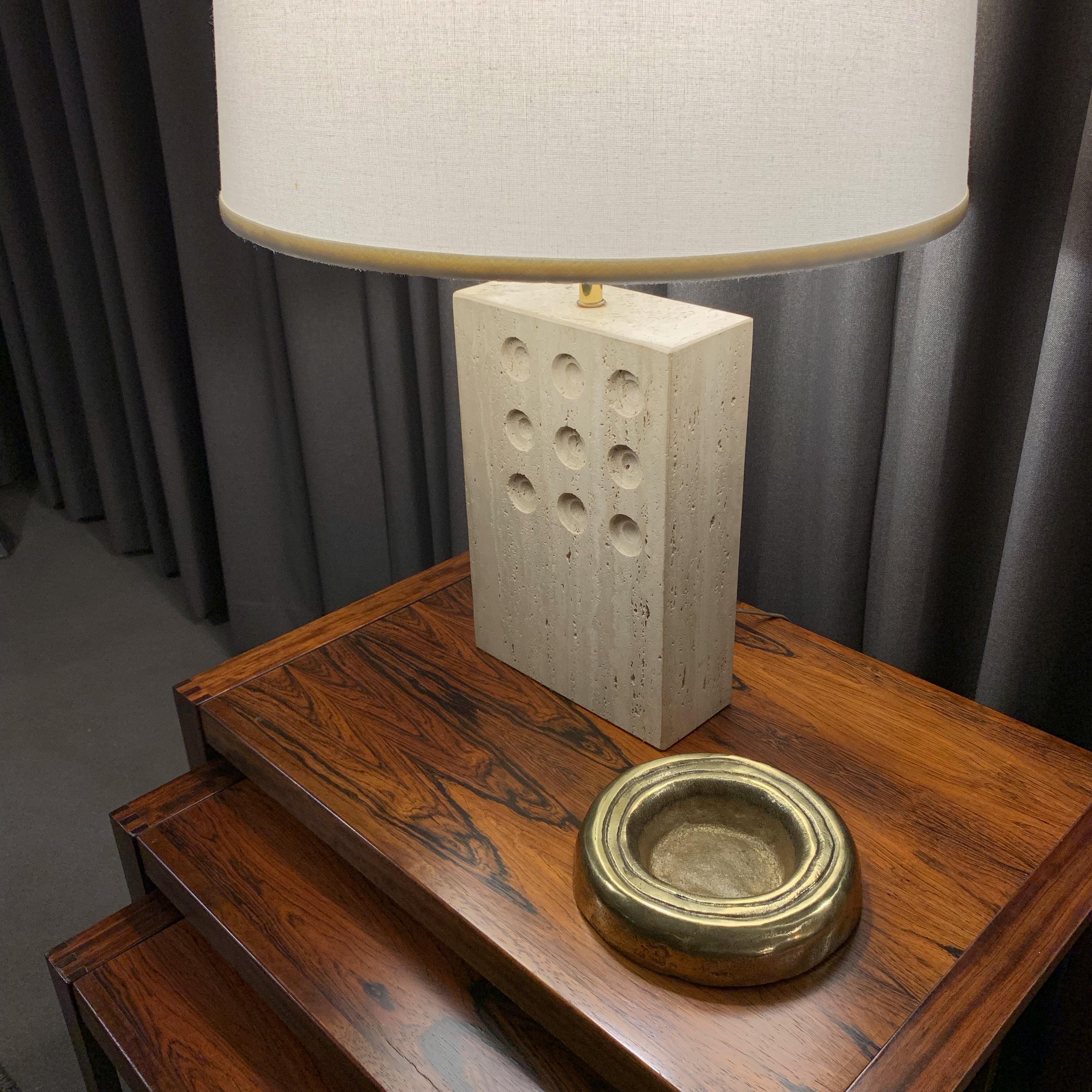 Stunning Italian travertine table lamp by Goffredo Reggiani for Raymor, circa 1960s. Solid travertine lamp with a grid of 9 carved / impressed circular designs. Brass stem, harp and finial. Takes one standard base light bulb. Working condition. Sold