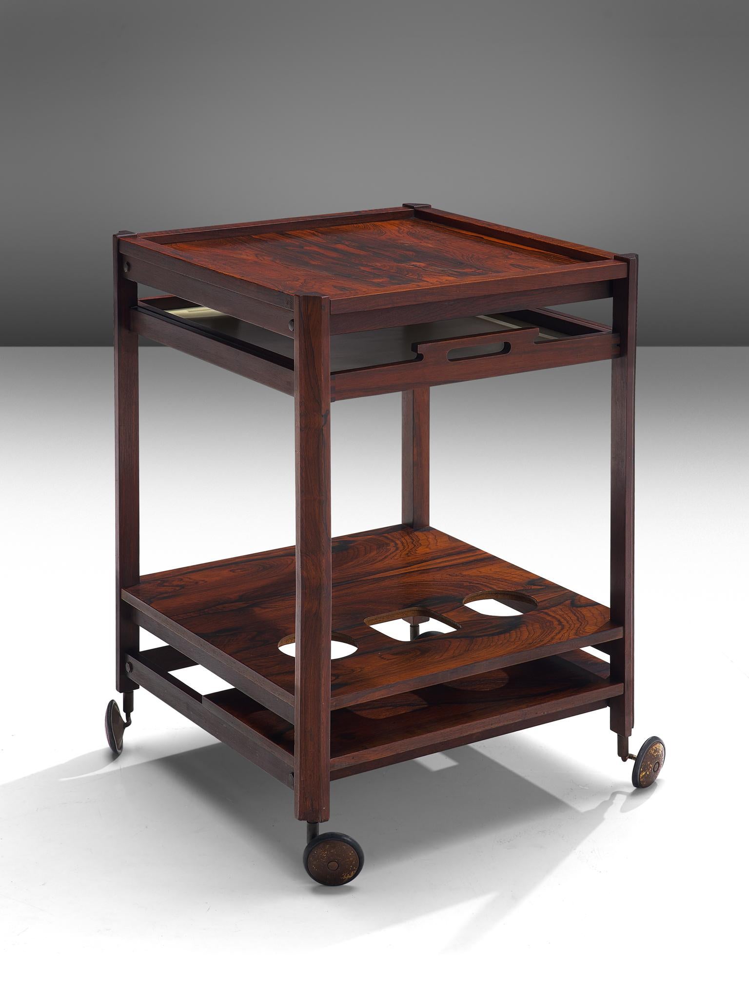 Trolley, rosewood, metal, Italy, 1960s.

This bar cart has been completely executed in rosewood veneer, resting on elegant brass wheels. The piece has several levels, with one pull-out tray and a tray with cut-outs to place bottles. The natural