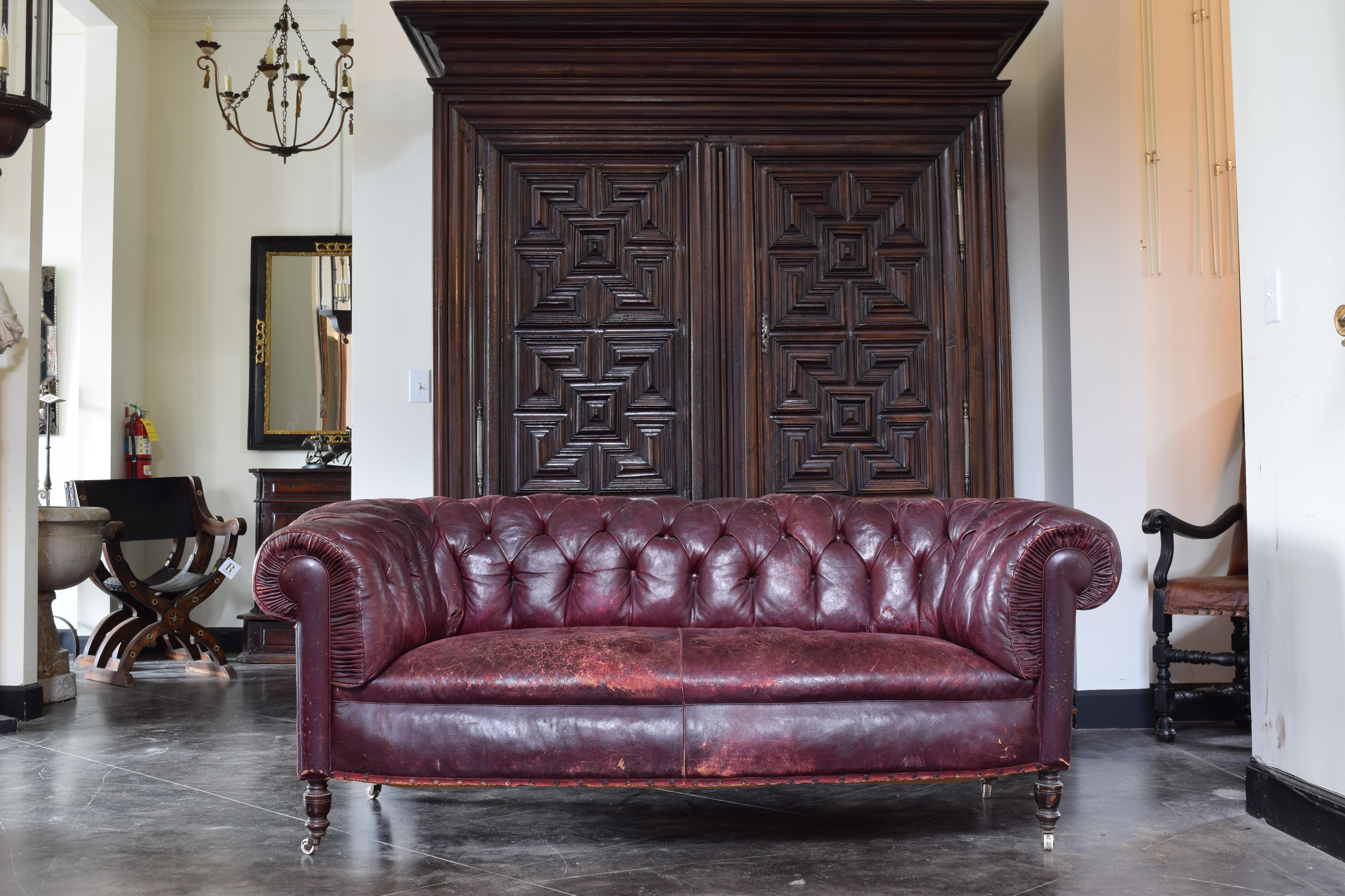 Beautifully worn chesterfield style sofa with a deep seat and tufted back and arms, the front of the arms with an interesting crimped leather, tight seat, raised on turned ebonized walnut feet with original casters, marked 