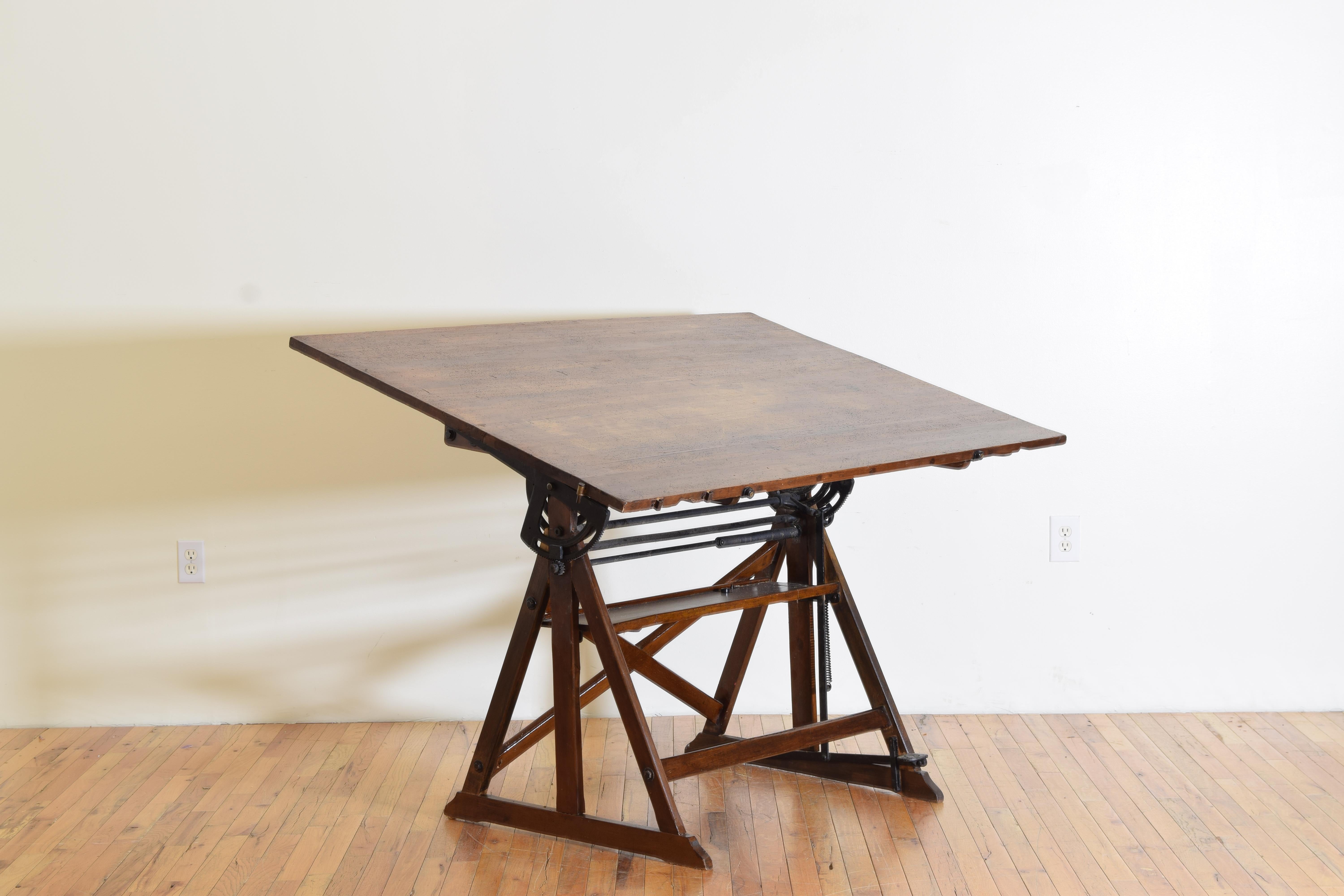 completely functional, having a large working surface atop triangular trestle form legs on bracket feet and a tray at mid height acting as a stretcher, within the frame is an elaborate iron adjusting system with a large counter-weight and a foot