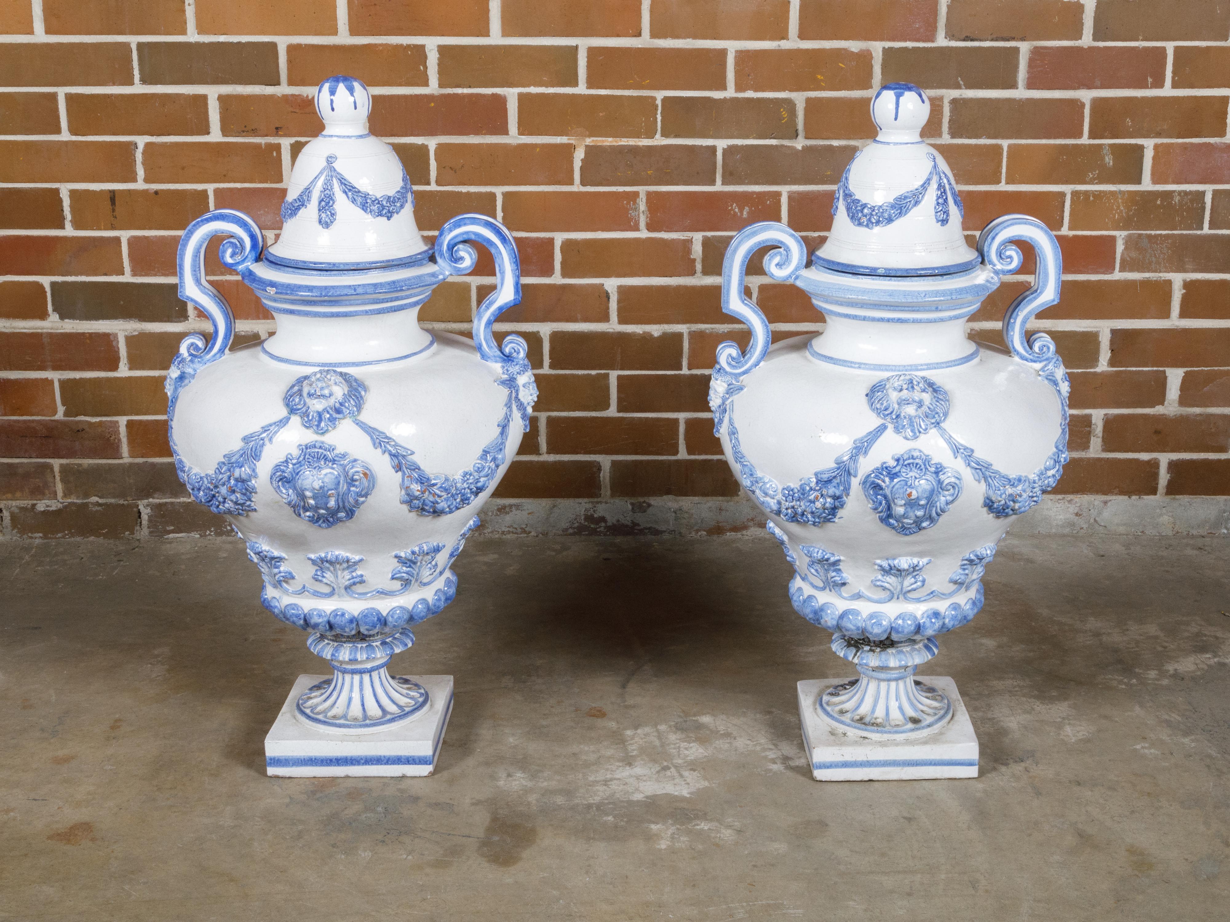A pair of Italian Turn of the century blue and white faience lidded jars from circa 1900 with faun motifs, volute handles, heraldic shields and lions. This exquisite pair of Italian faience lidded jars, dating back to the turn of the century circa