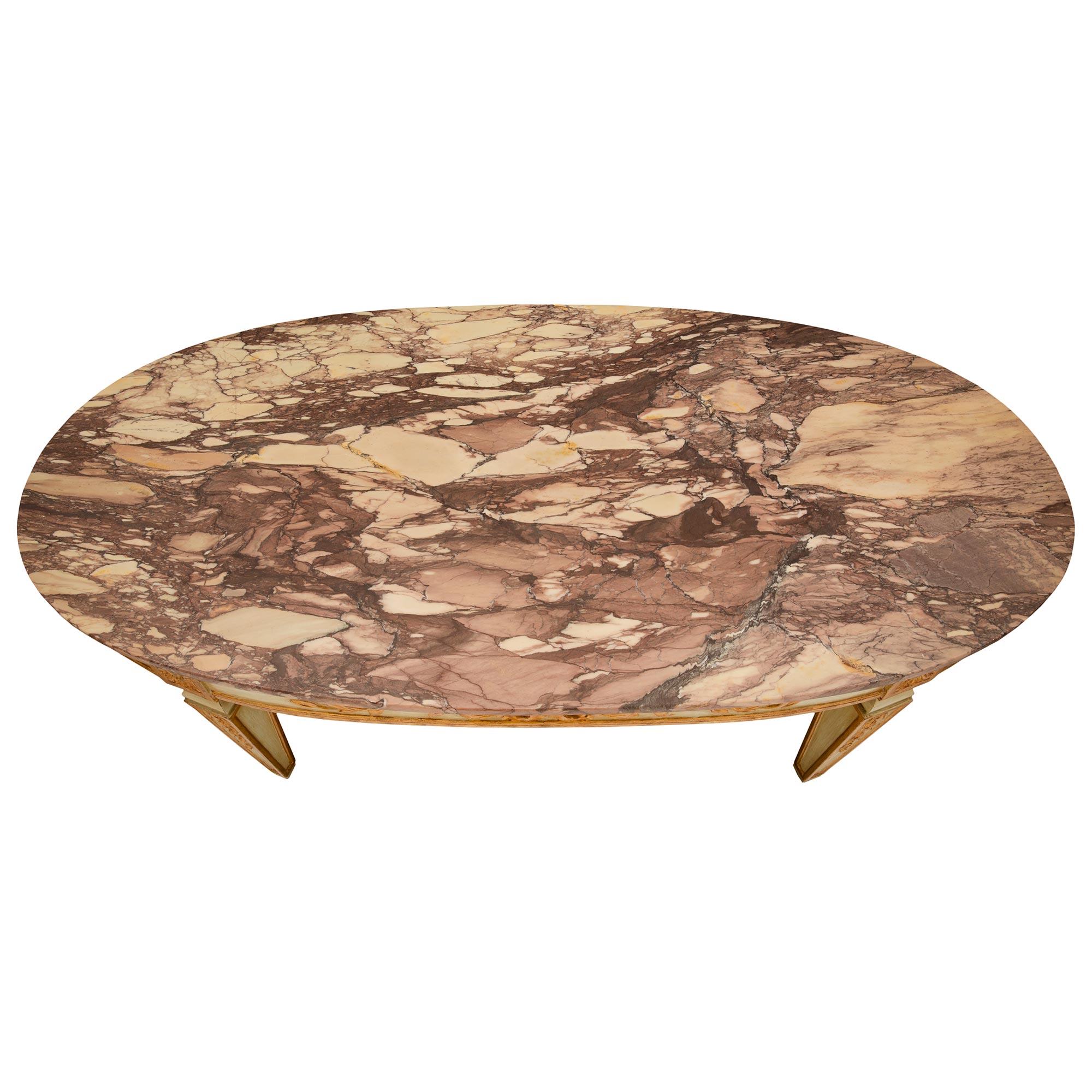 A beautiful Italian, turn of the century Louis XVI St. patinated wood, giltwood and Brèche violette marble coffee table. The oblong shaped table is raised by elegant square tapered legs with finely carved gilt foliate garlands framed within gilt