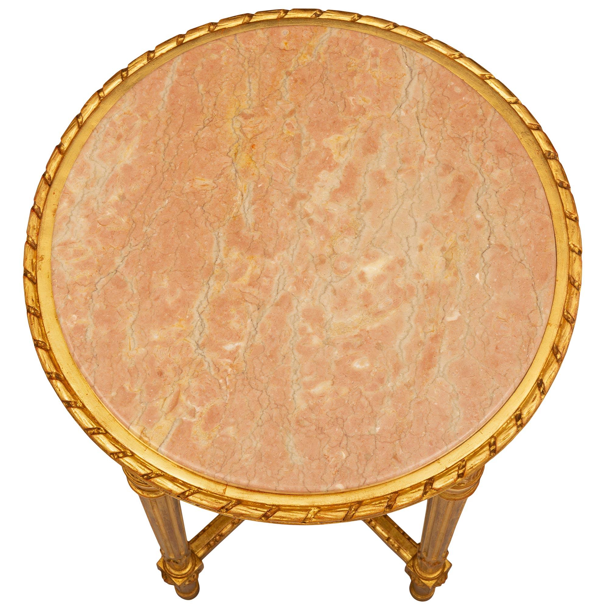 Ein sehr eleganter italienischer Beistelltisch aus dem Louis XVI Jahrhundert aus vergoldetem Holz und Rose Phocéen-Marmor. Der runde Tisch steht auf schlanken, kreisrunden, konisch zulaufenden, kannelierten Beinen mit hübschen, topieförmigen Füßen
