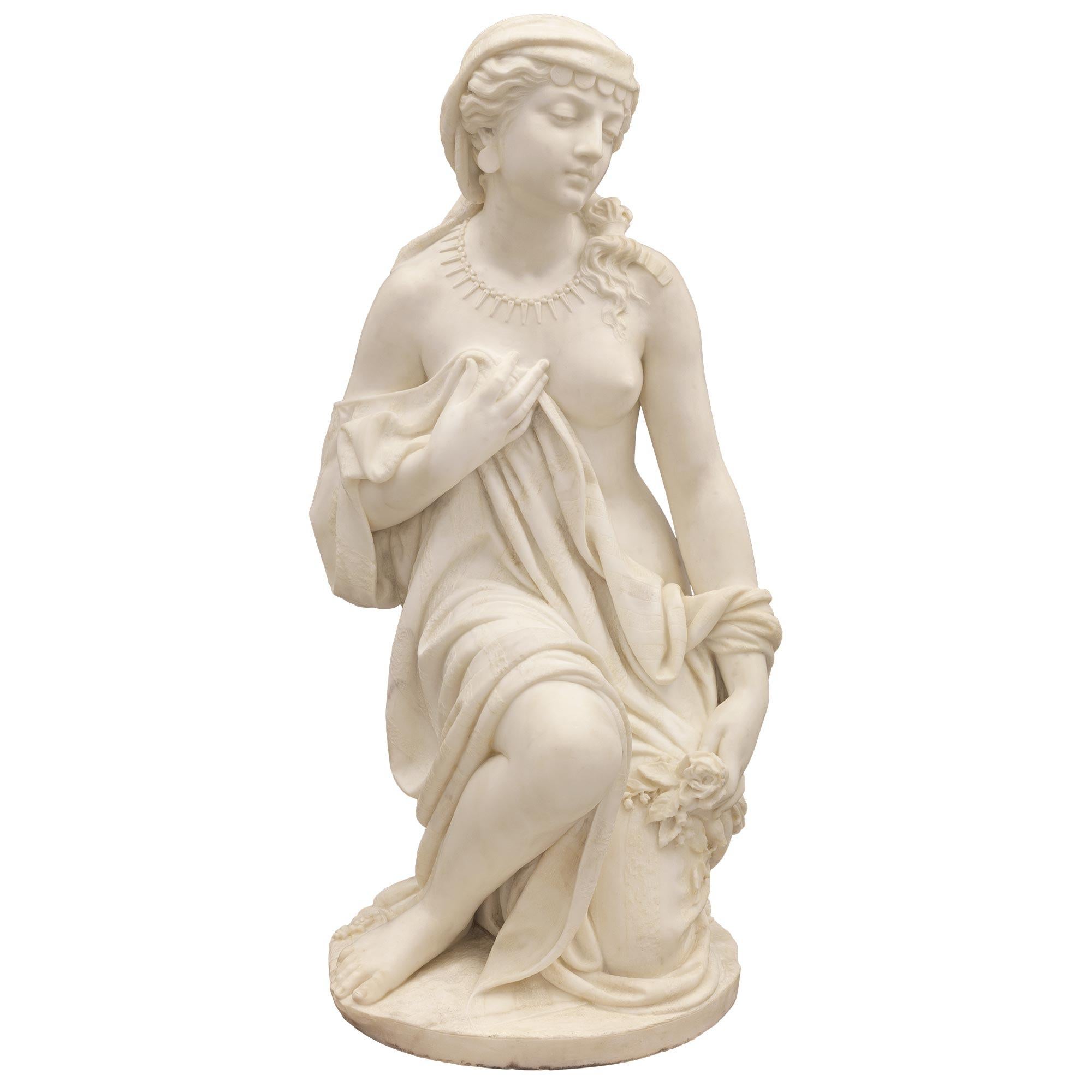 A stunning and very high quality Italian turn of the century white Carrara marble statue signed Prof. R. Romanelli 1909. The statue is raised by a circular base with a fine ground like design where the beautiful maiden is kneeling. She is draped in