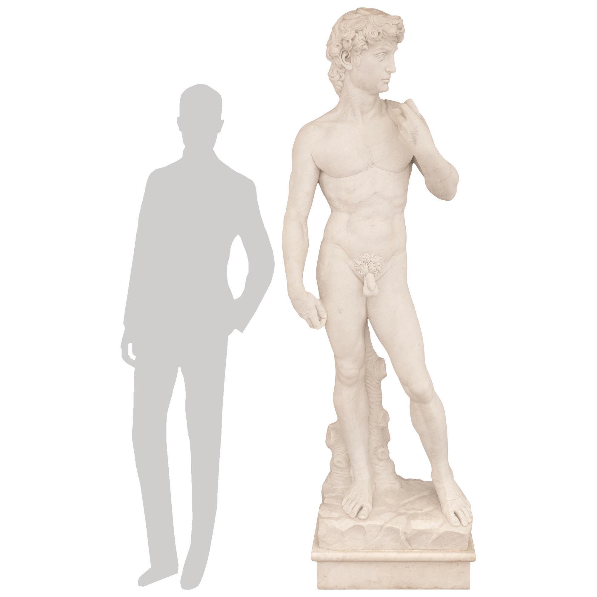 An impressive and high quality Italian turn of the century white Carrara marble statue of Michelangelo's David. This iconic and world renowned statue is supported on a square mottled marble base with a ground like platform above. Atop the earthly