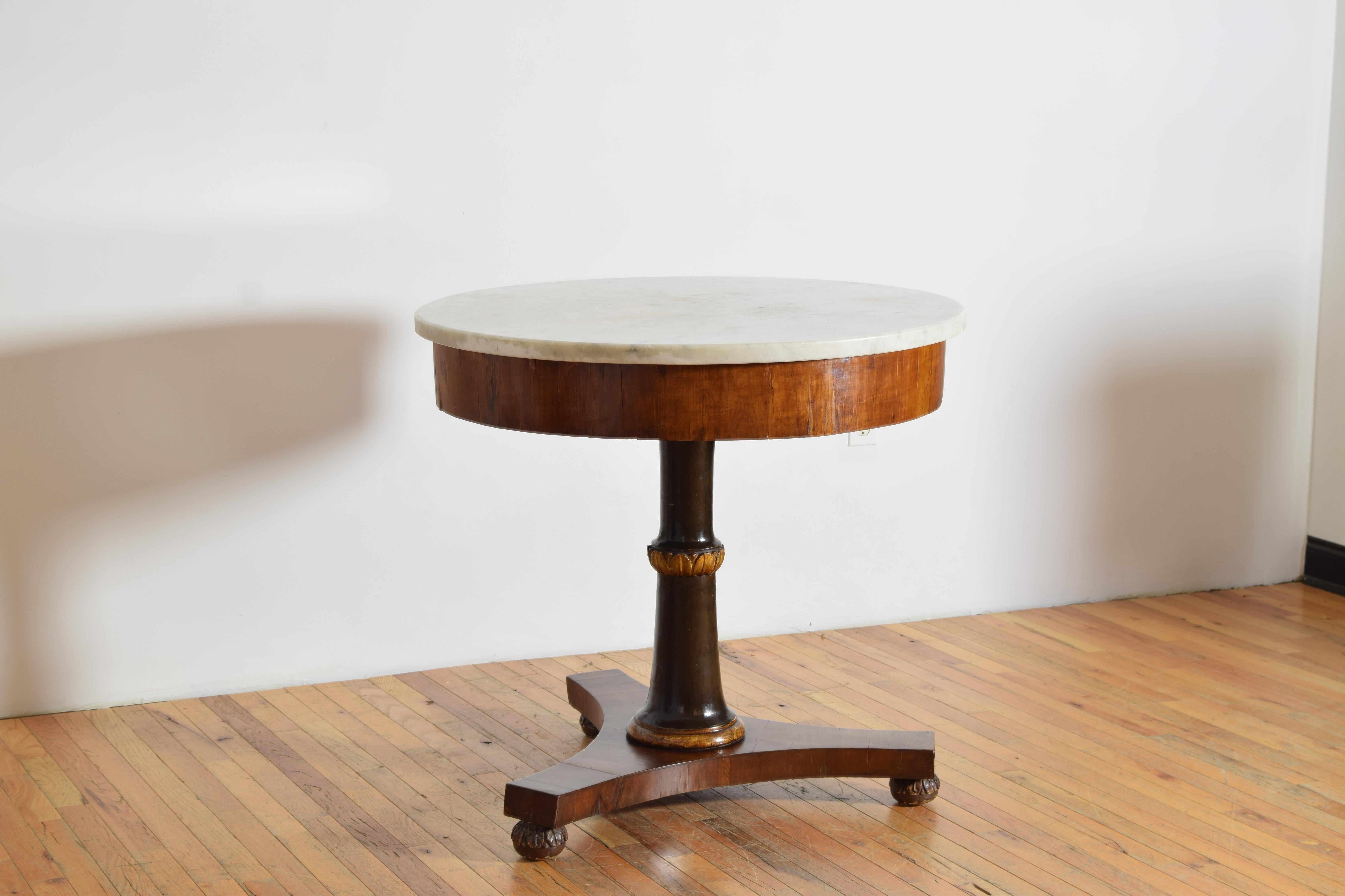 Having a thick circular Carrara marble top above a veneered apron atop an ebonized standard with carved giltwood rings, the tripartite base issuing covered in veneer and raised on carved giltwood feet