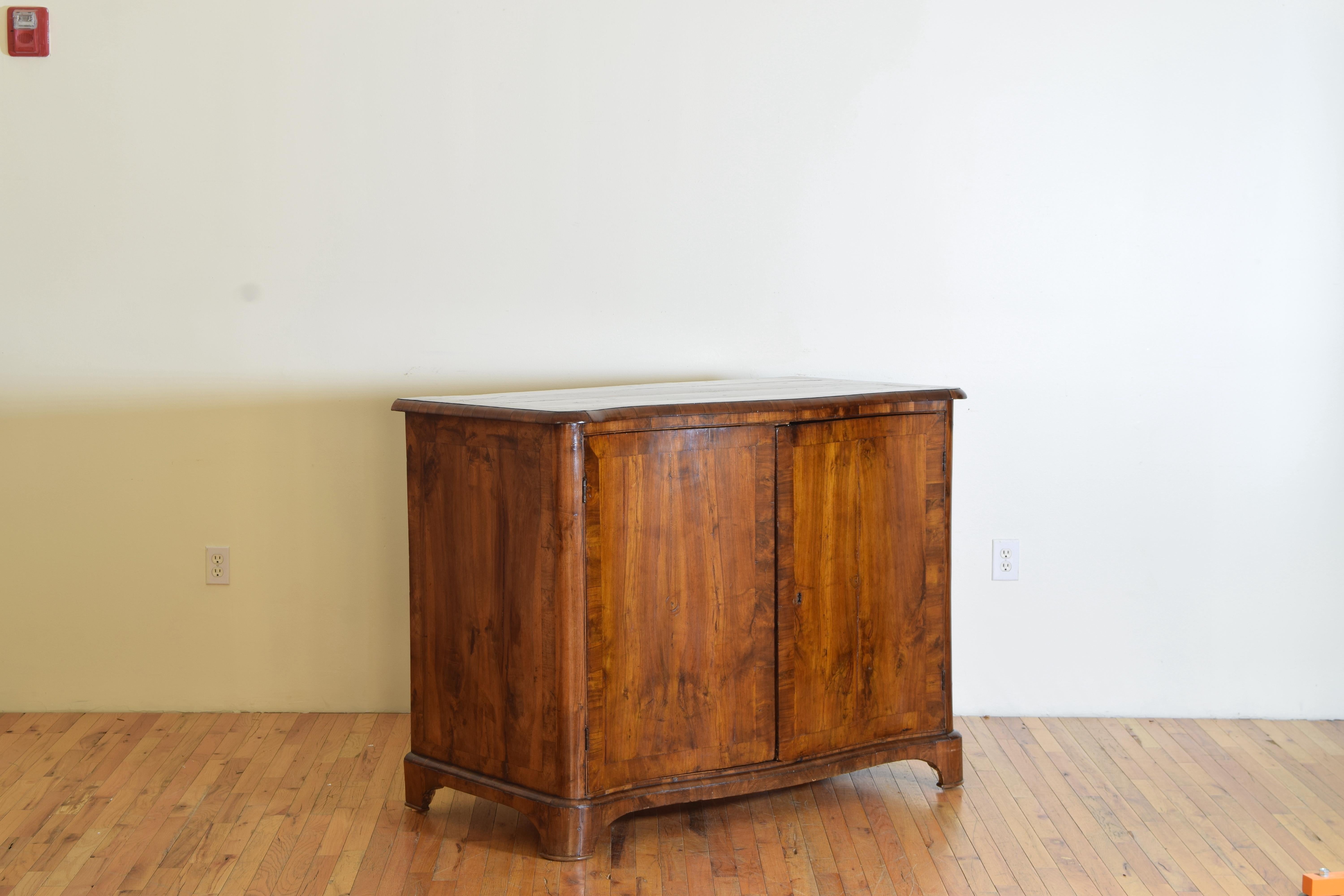 A walnut and veneered walnut banded inlay sideboard or cabinet having a slight bombe or curved front resting on open bracket feet. The interior having sizable depth and slides instead of drawers for storage.
 