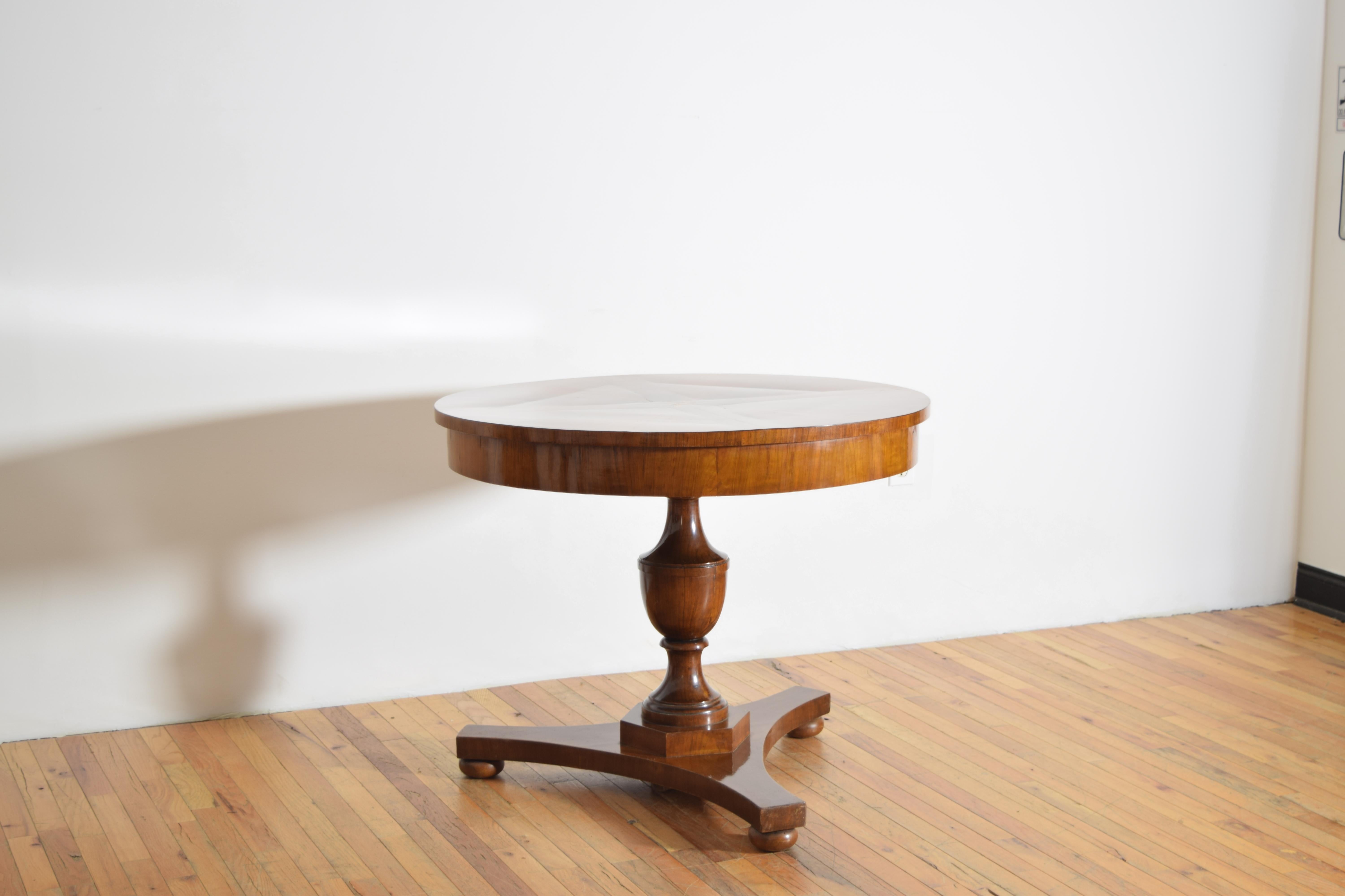 constructed of solid walnut and walnut veneers, both of the lighter shade with a deep patina this table has a circular top with matching wedge veneers and a centered light wood inlaid rosette above a deep apron, the turned solid walnut standard with
