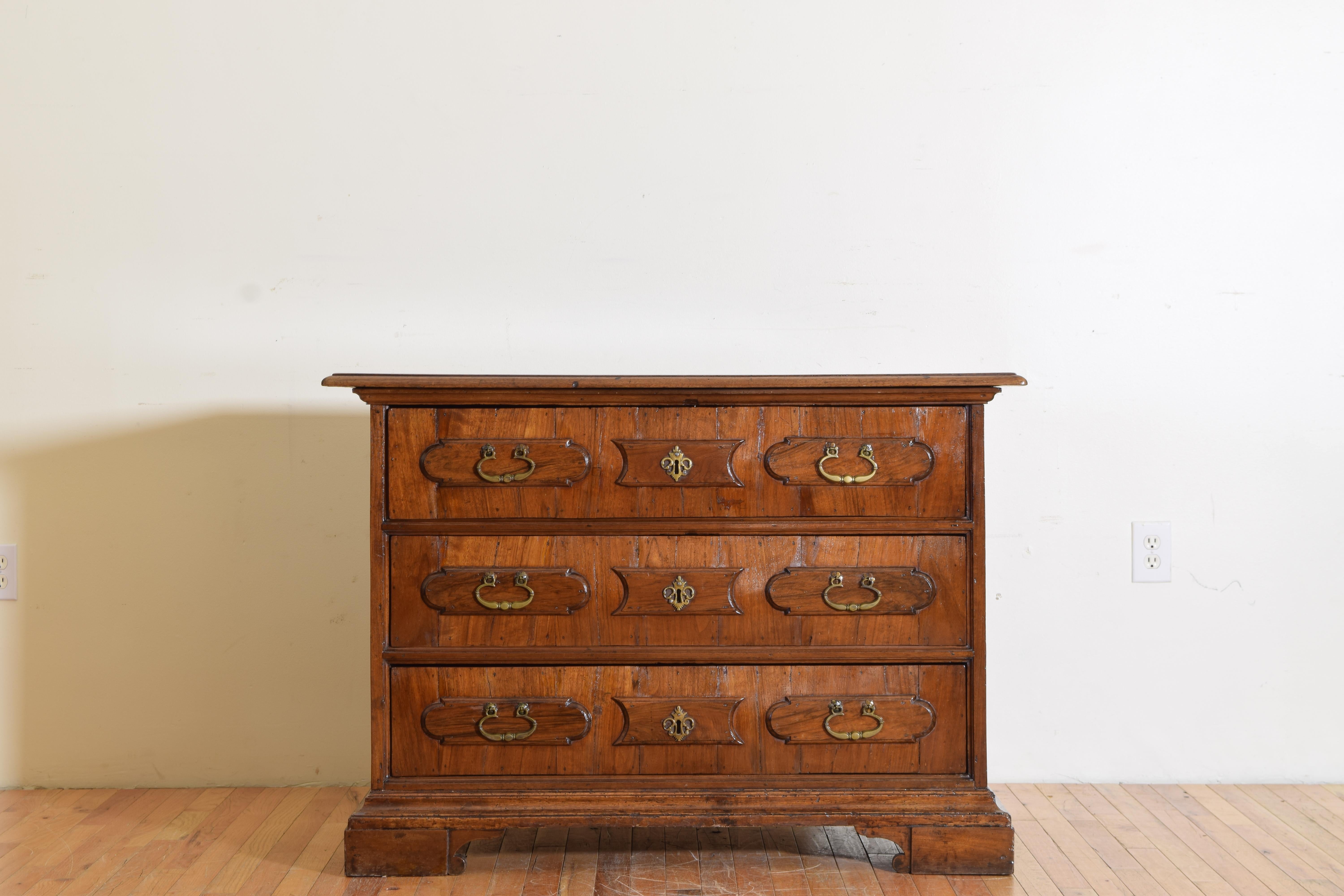 Having a wonderful polished veneered patina with bronze hand pulls and escutcheons, this three-drawer commode has raised panels on the sides as well as on the drawer fronts.  Raised on a hand-carved plinth base.