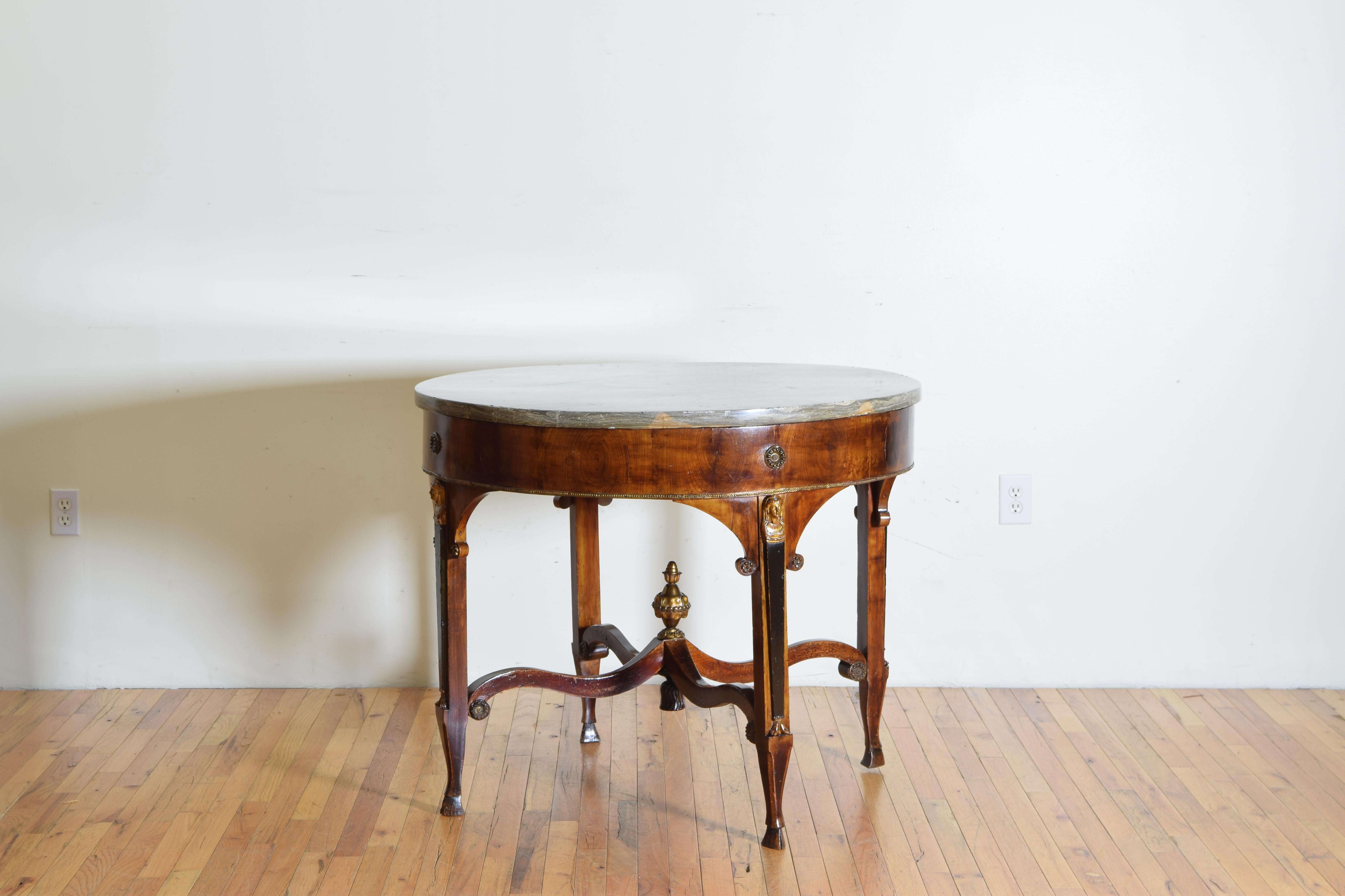 Having its original handcut marble top atop a circular frame with a veneered apron adorned with brass rosettes, the legs with arched top and rosettes, the fronts ebonized and having giltwood caryatids, the arched stretchers with a brass finial and