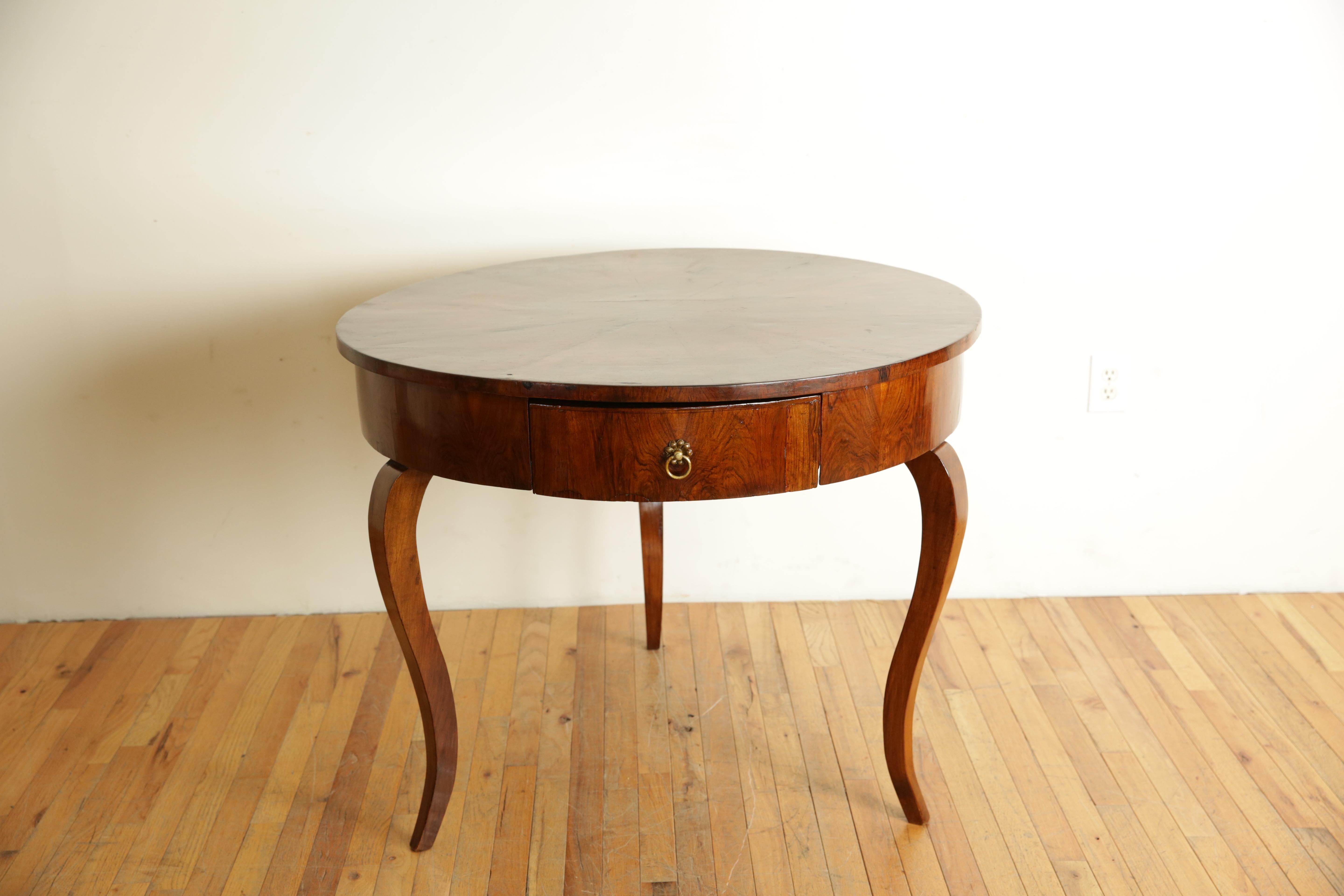 The table covered completely in figured walnut veneers with a circular top with sector shaped veneers, the conforming case housing one drawer with its original brass pull, the table raised on curved and tapering legs