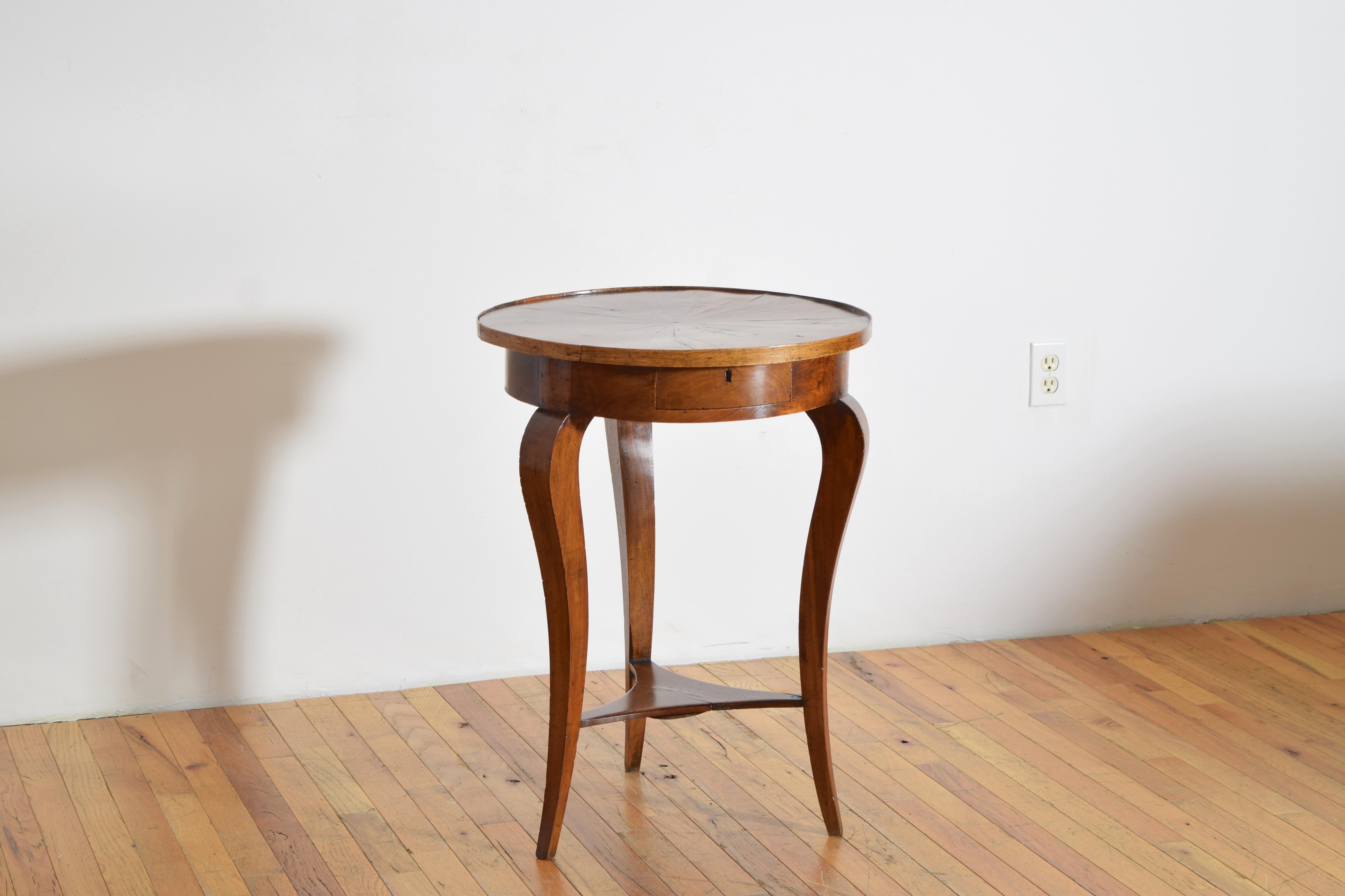 the circular top radially veneered and having a raised gallery edge, the case housing one drawer and raised on shaped and tapering legs, the legs joined by a shaped stretcher at the lower level