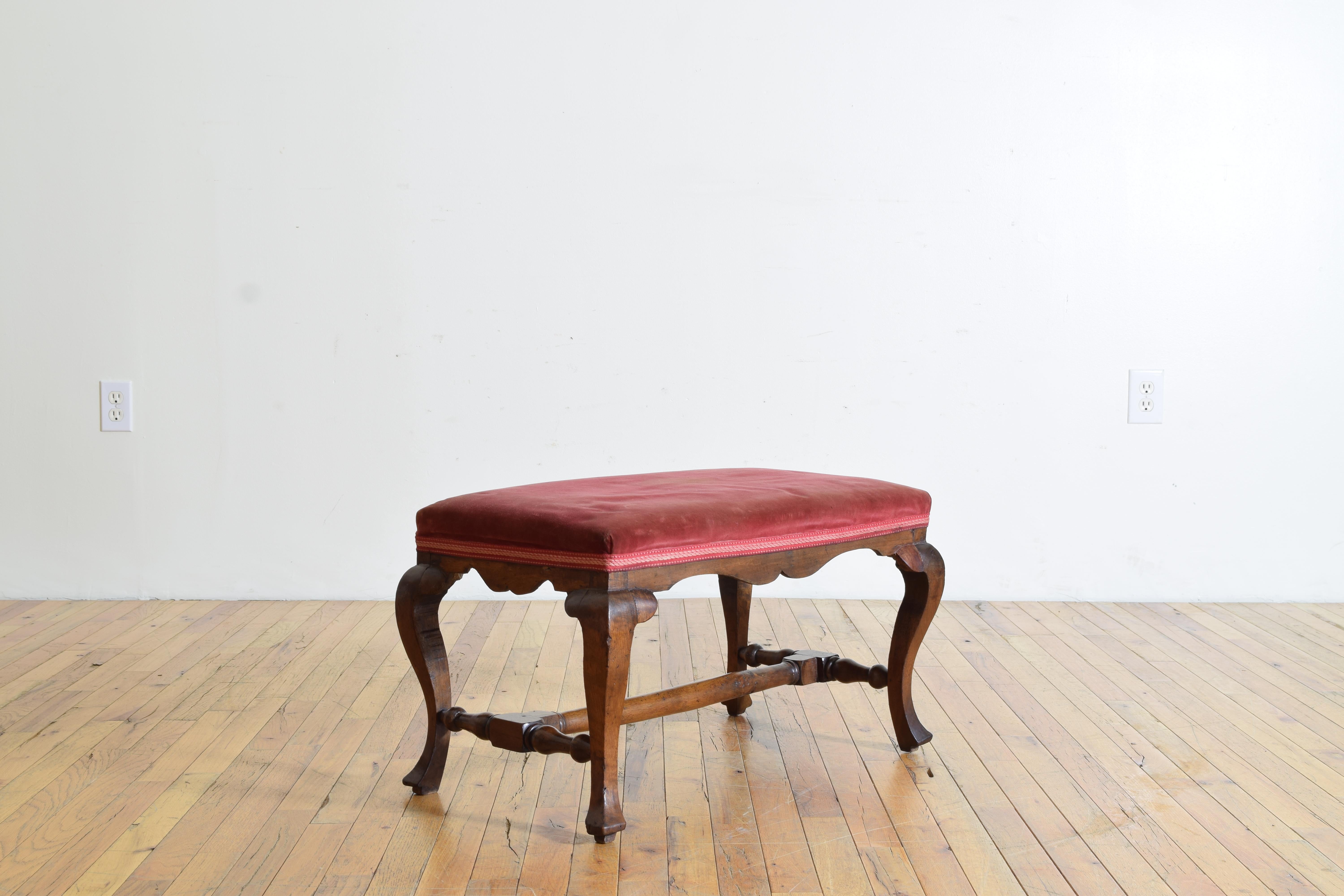 Retaining its vintage velvet upholstery on its rectangular top, with a shaped apron and raised on cabriole legs joined by a turned stretcher, the shaped feet slightly raised