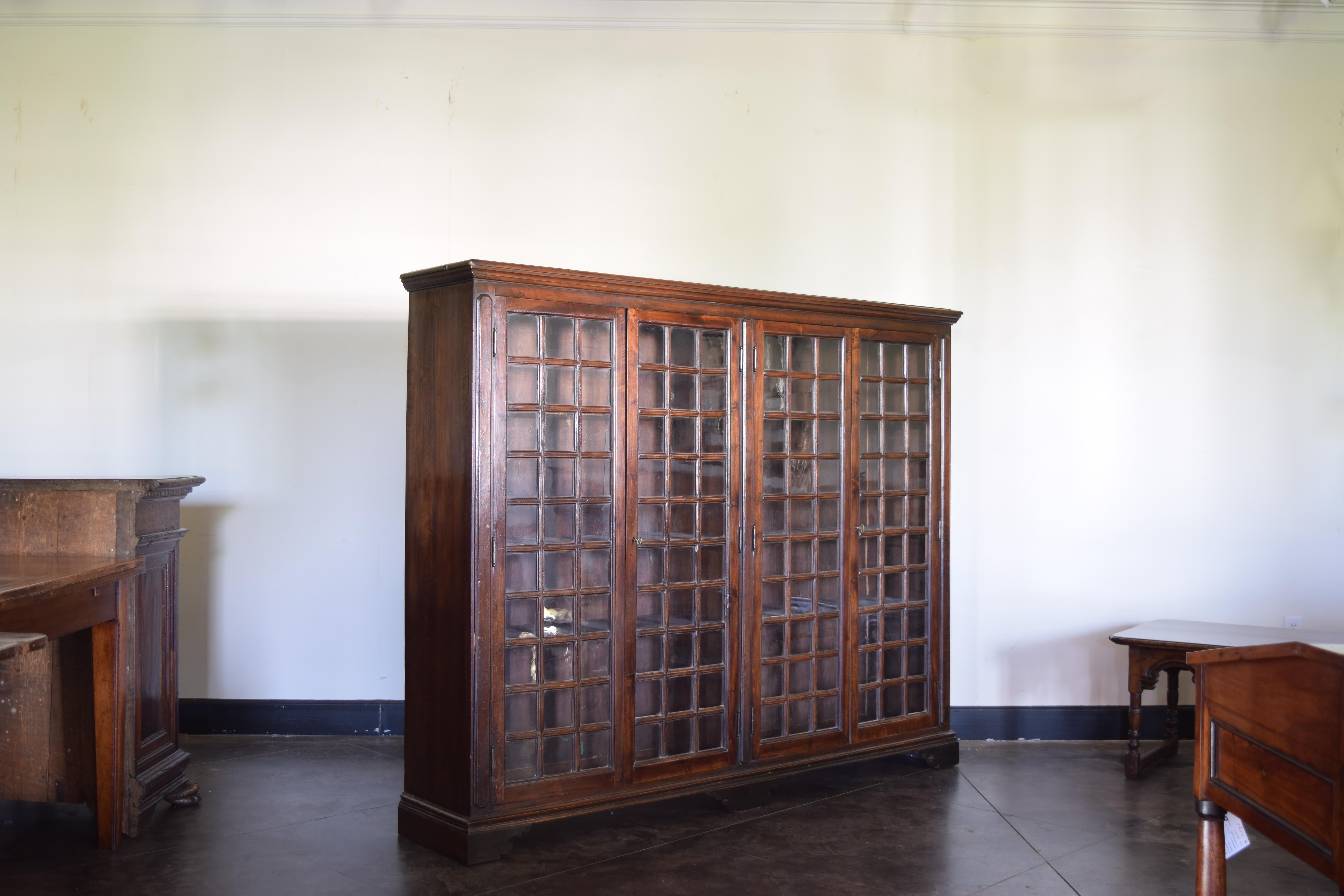 avec une corniche au-dessus d'une caisse conforme avec quatre portes, chacune avec des fenêtres en verre séparées, encadrées par des pilastres façonnés sur les côtés avant et au centre, l'intérieur avec des étagères, reposant sur une base en forme