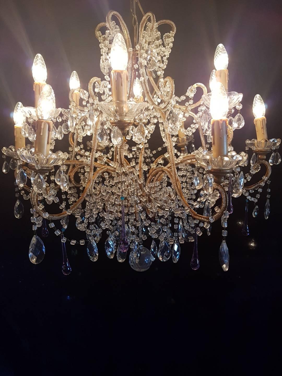 Italian gilt iron chandelier with 12 arms. Gilt iron frame is covered with beads. The bobeches with candle lights are being carried by wood. A few light purple glass drops with a blue bead are giving a really nice effect to the chandelier. The