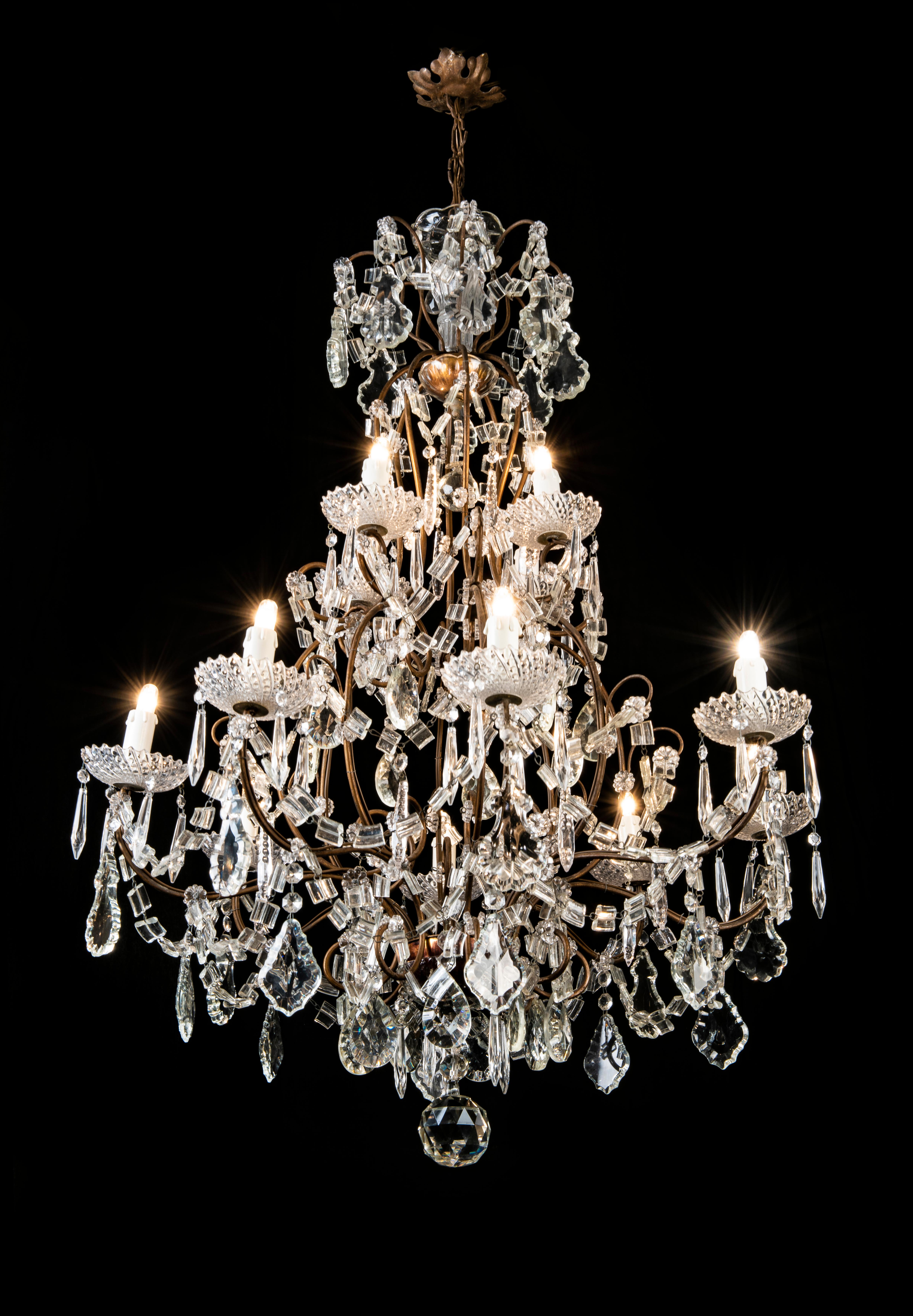 An Italian two-tiered chandelier with a partially gilt iron cage shaped frame, with a lovely antique dark patina. The chandelier is dressed with good quality crystal pendants, the twelve-light curved arms are in two tiers 8 + 4 and issue crystal