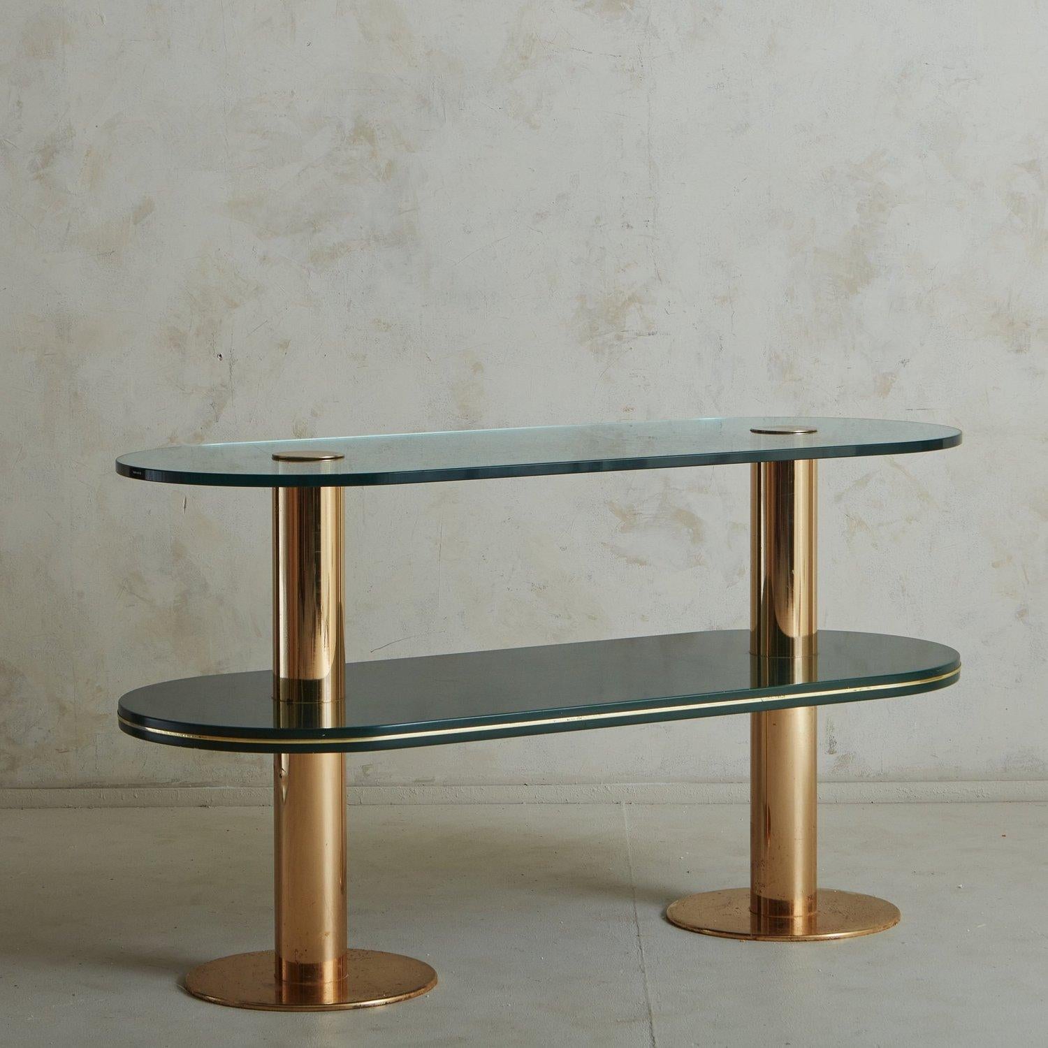 A vintage Italian console table featuring a brass frame with two cylindrical legs and dramatic circular feet. This piece has two tempered glass shelves with curved edges in a beautiful green hue. The bottom shelf is a darker tone and has an elegant
