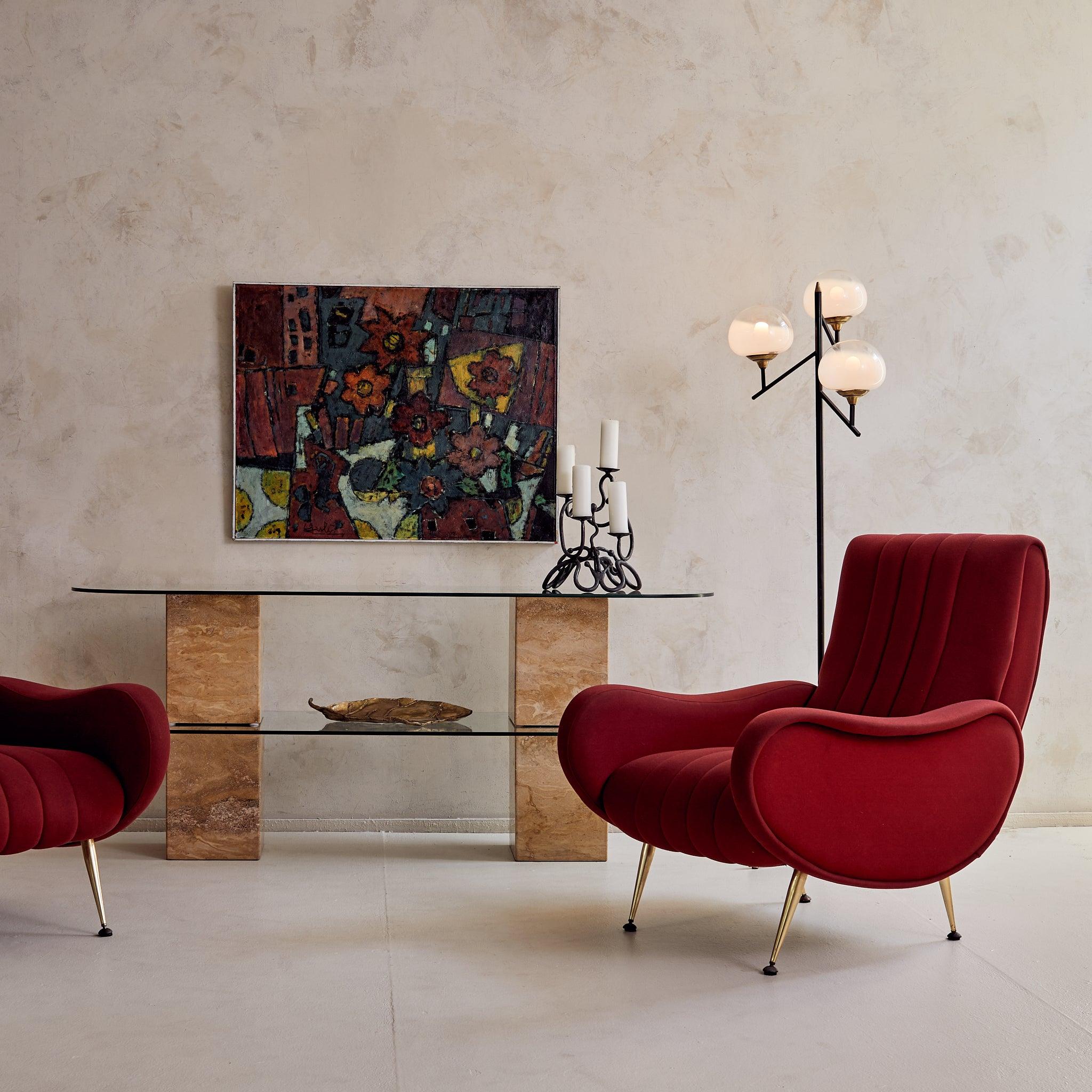 An Italian console table from the 1970s, anchored by four solid travertine pedestals. The organic variation in the stone, ranging from deep ochre and ivory to creamy taupe, adds warmth and movement to the geometric form. Two pill-shaped glass tiers