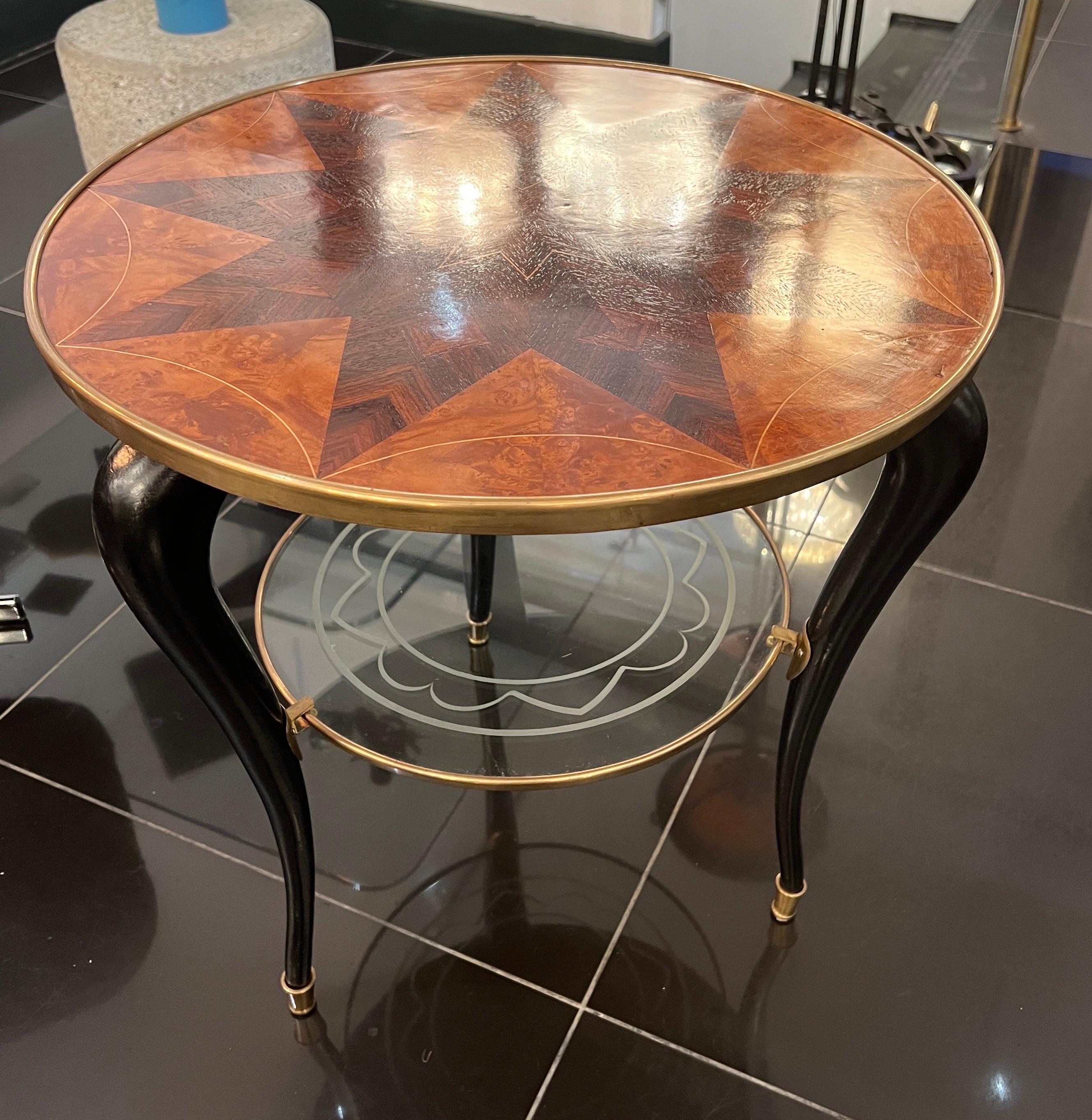 A fabulous Italian two tiered circular side table with beautiful  walnut marquetry design on top surrounded by a brass frame .. The lower section is etched glass also supported by a brass frame . There’re three curved legs in black lacquer with