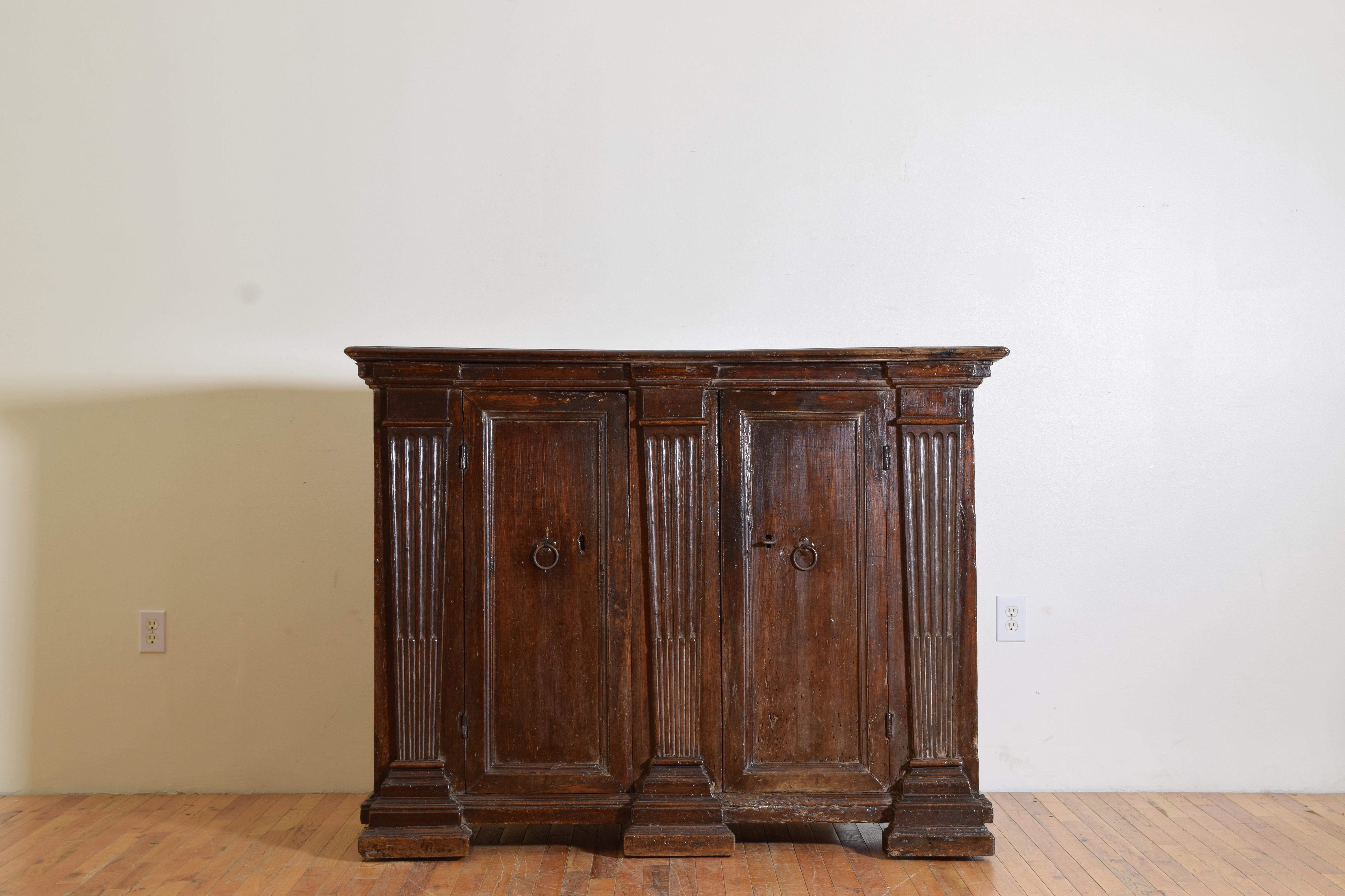 having a rectangular top with molded edge atop a conforming case with two doors housing interior shelving, the doors centered among tapering fluted pilasters with pronounced capitals and bases, raised on a layered plinth base, original locks and key
