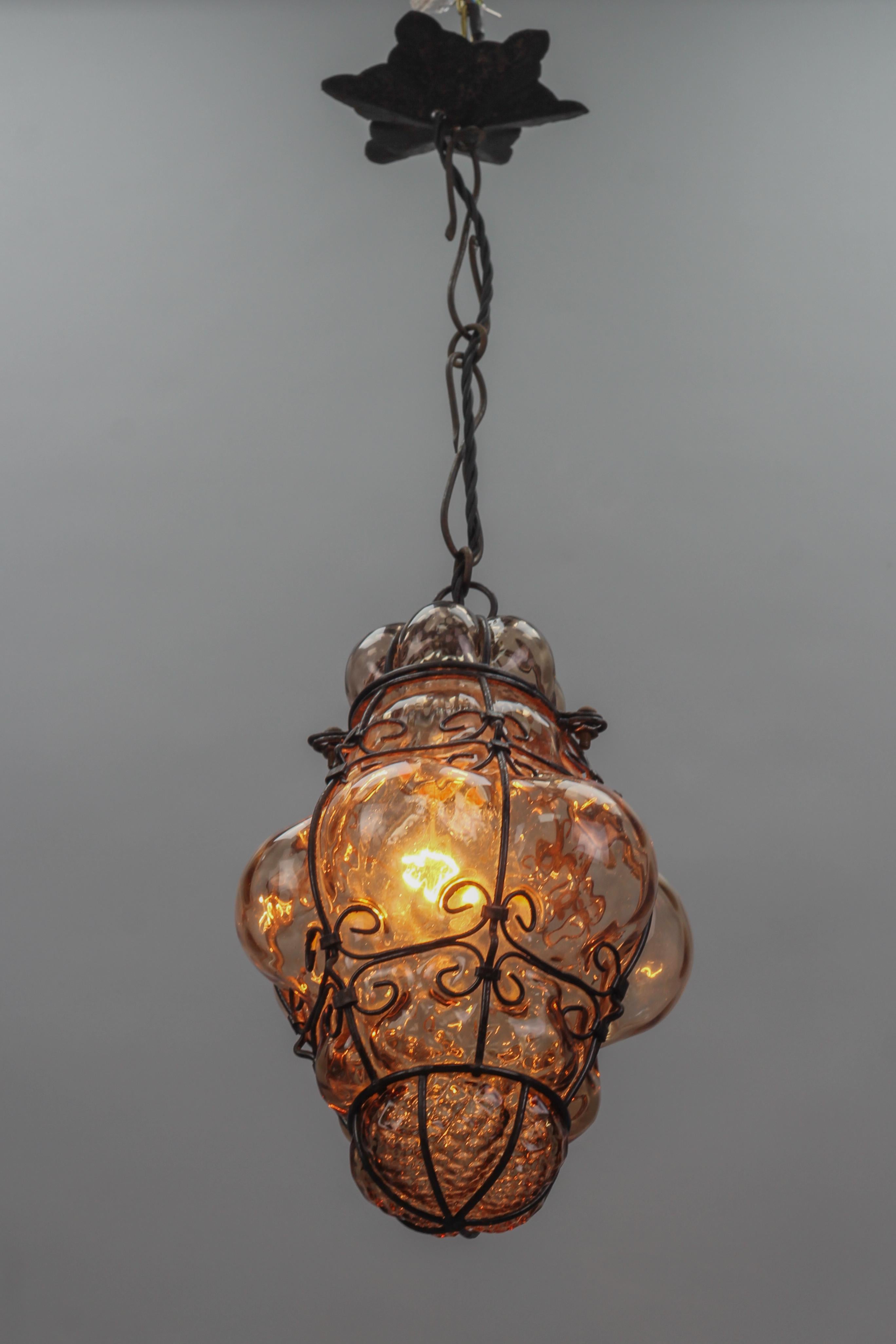 Italian Venetian amber smoke coloured clear murano glass caged lantern.
This beautiful Italian hanging lantern features clear amber smoke-colored Murano glass captivated within a metal frame. The bulbous form is produced when the glass is blown